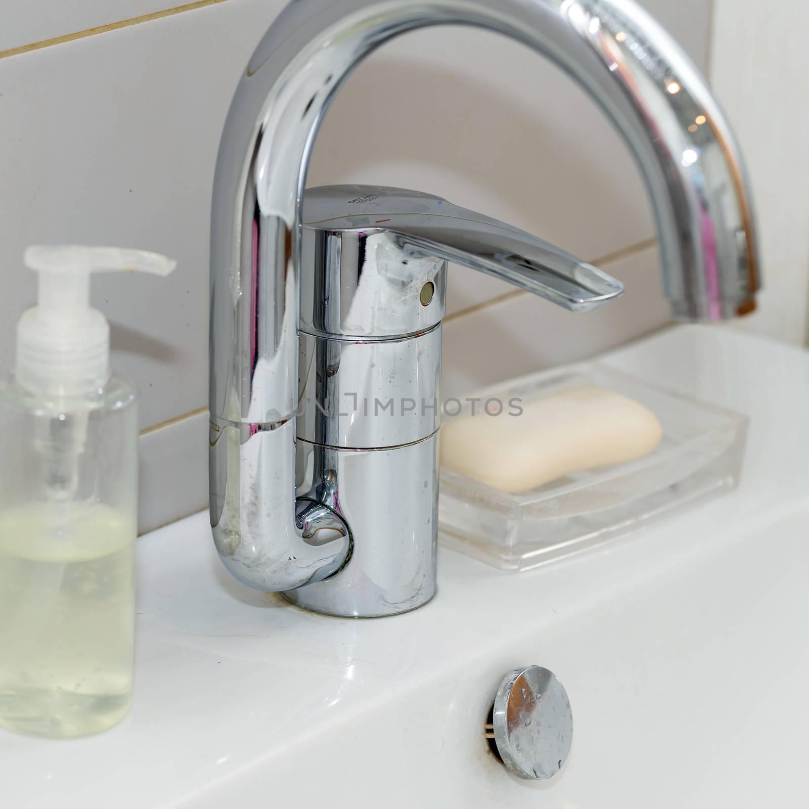 Modern hand wash basin. Solid tabletop surface and gray tile wall. Dispensable soap next to water tap on bathroom sink