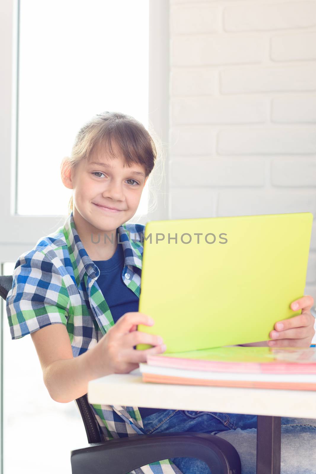 A girl with a tablet sits at a table at home and joyfully looked into the frame
