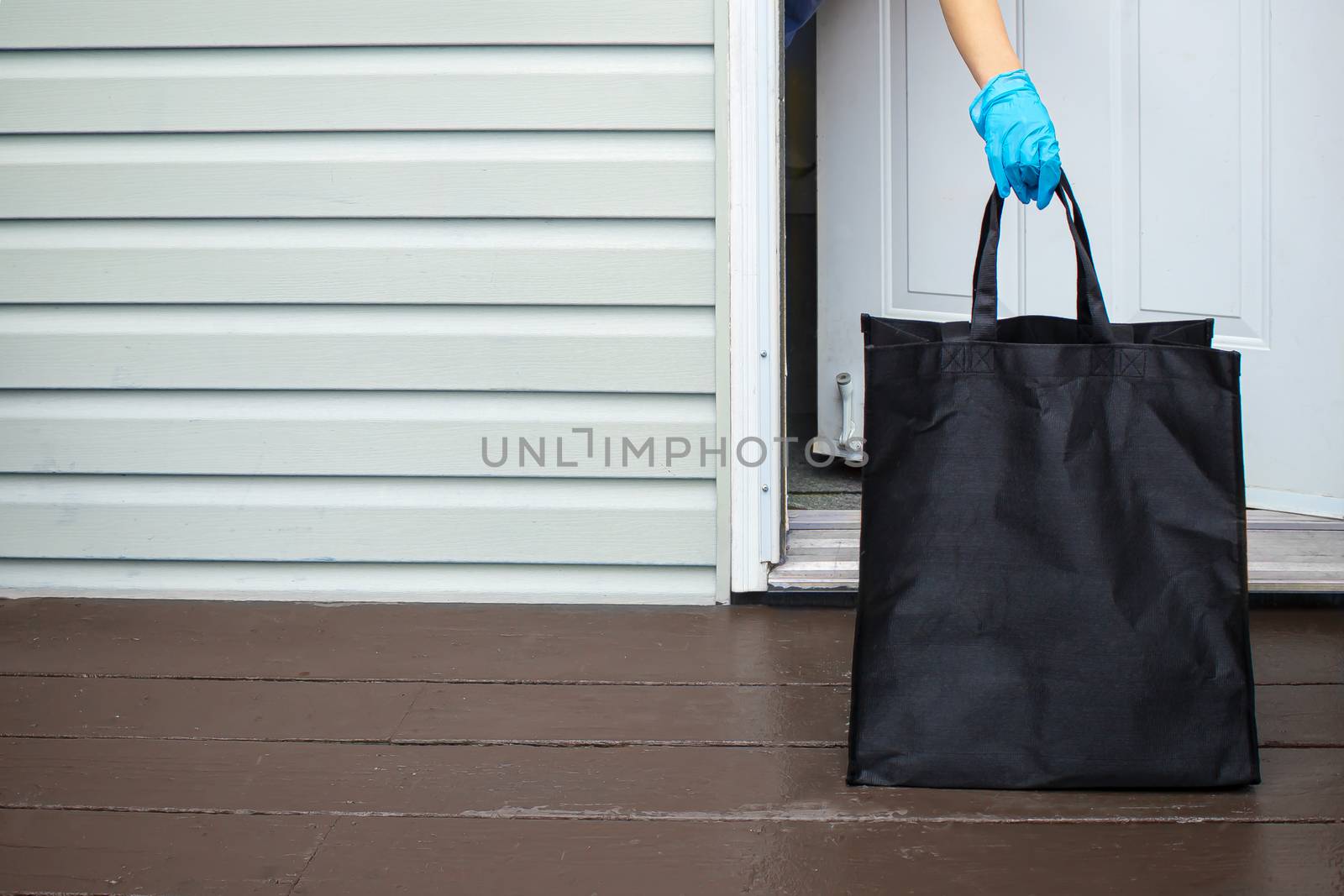 A person wearing gloves, picking up a groceries bag from a home entrance by oasisamuel