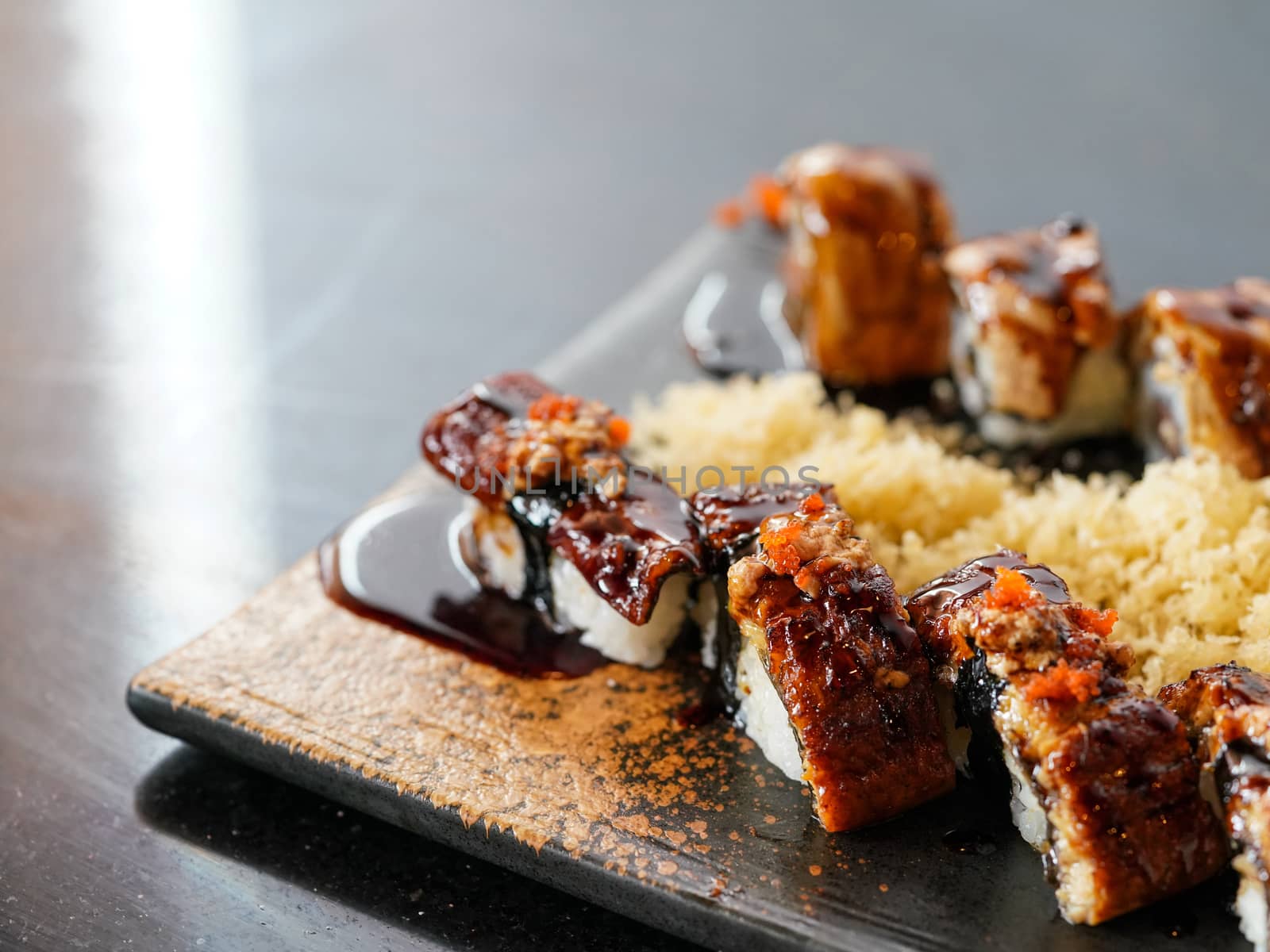 Anago sushi topped with Foie Gras, served with tempura crust on a black plate. Japanese Cuisine Buffet.
