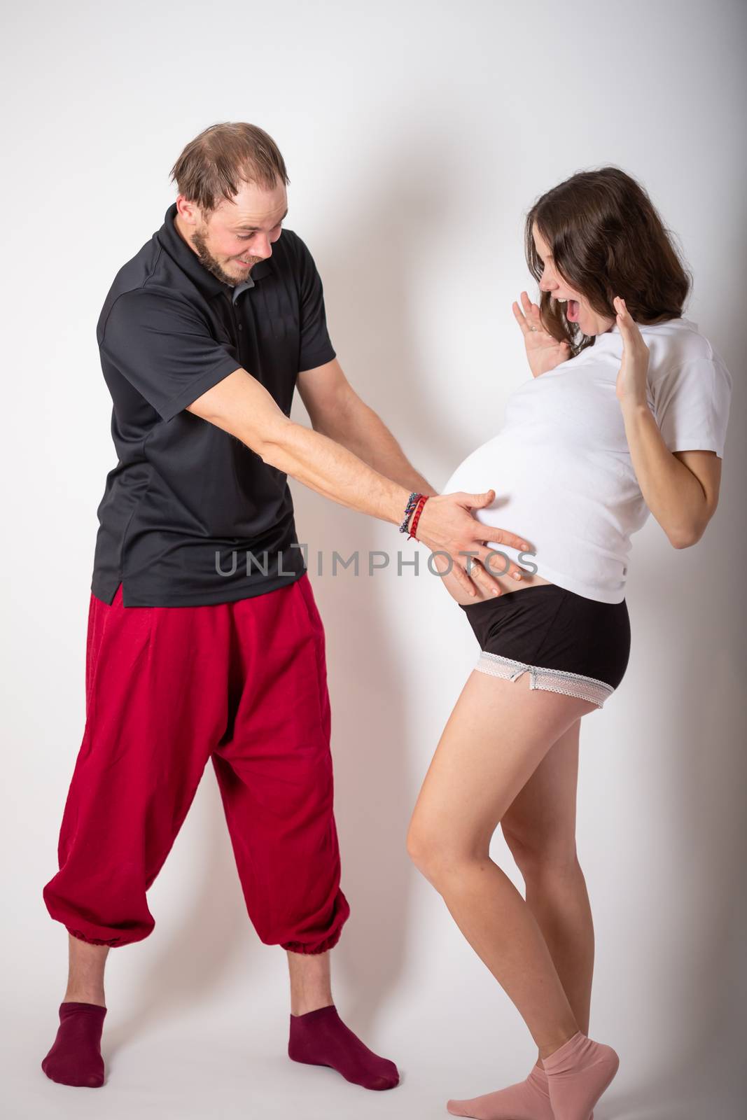 Handsome man is listening to his beautiful pregnant wife's tummy and smiling.