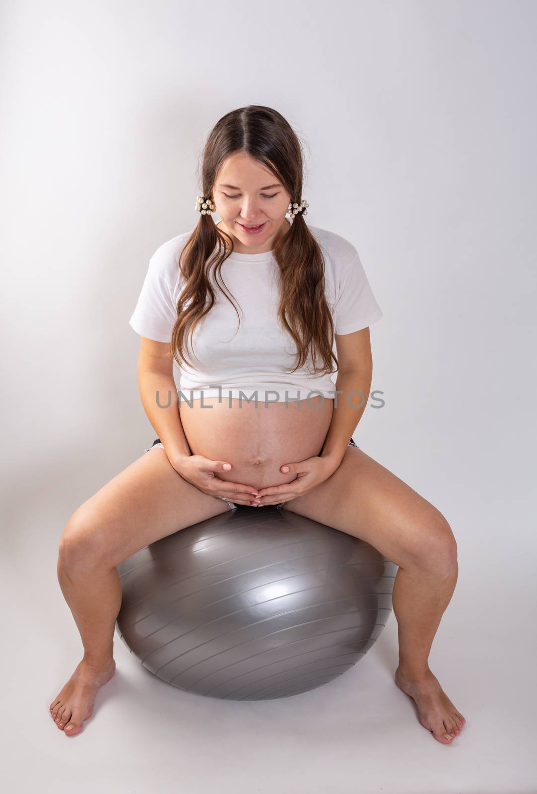 A pregnant young woman is doing on fitball.