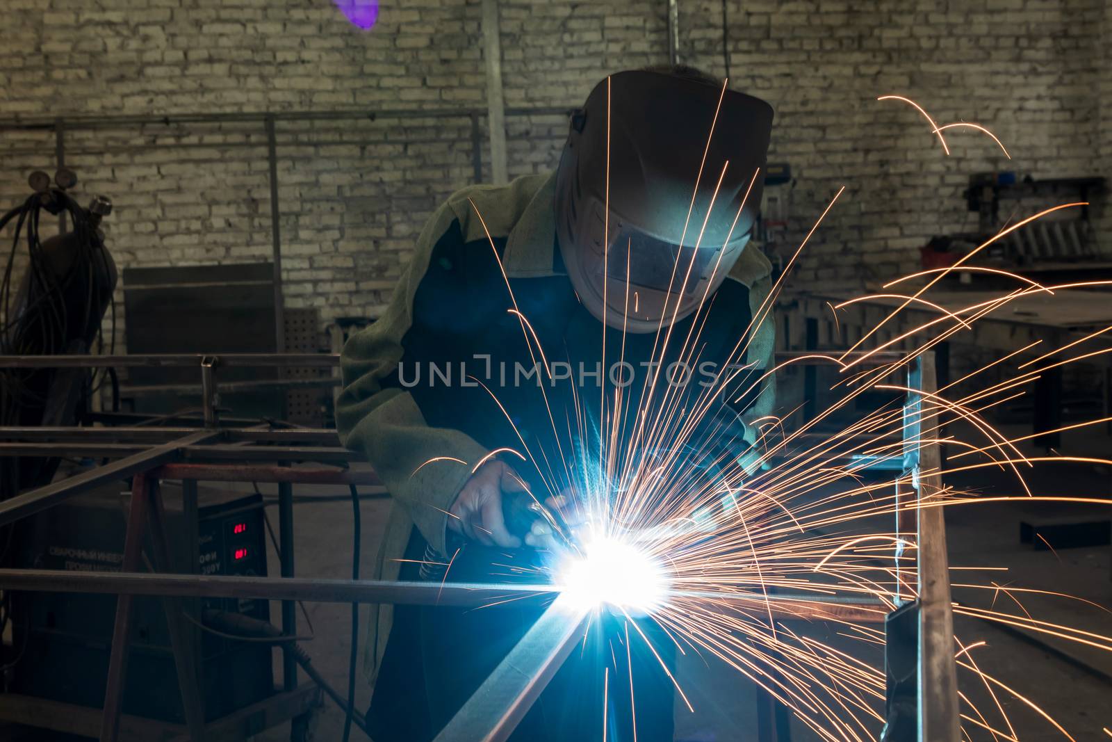 Welder welding a metal part in an industrial environment, wearing standard protection equipment. by sveter