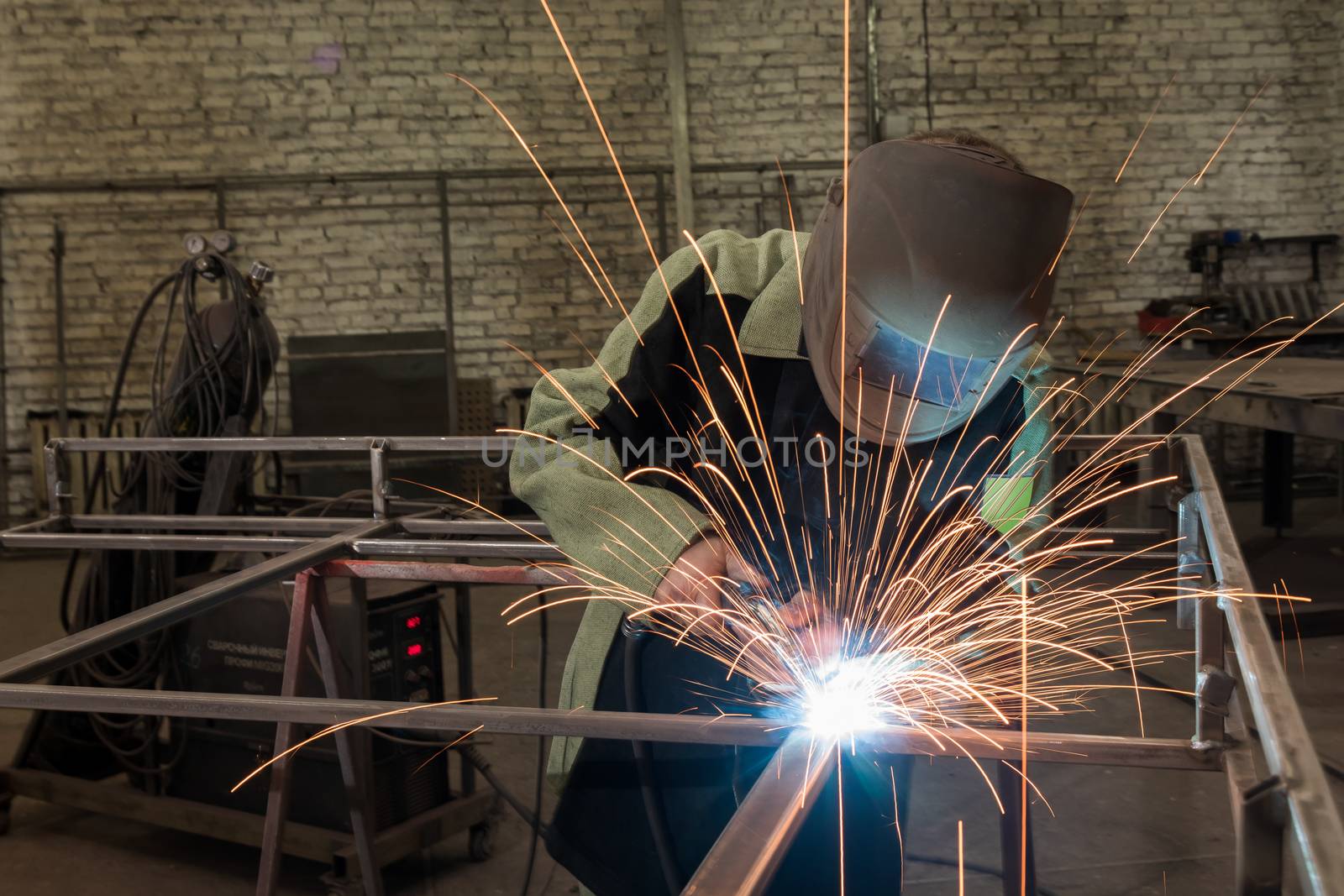 Welder welding a metal part in an industrial environment, wearing standard protection equipment. Sparks flying, fumes, industrial background