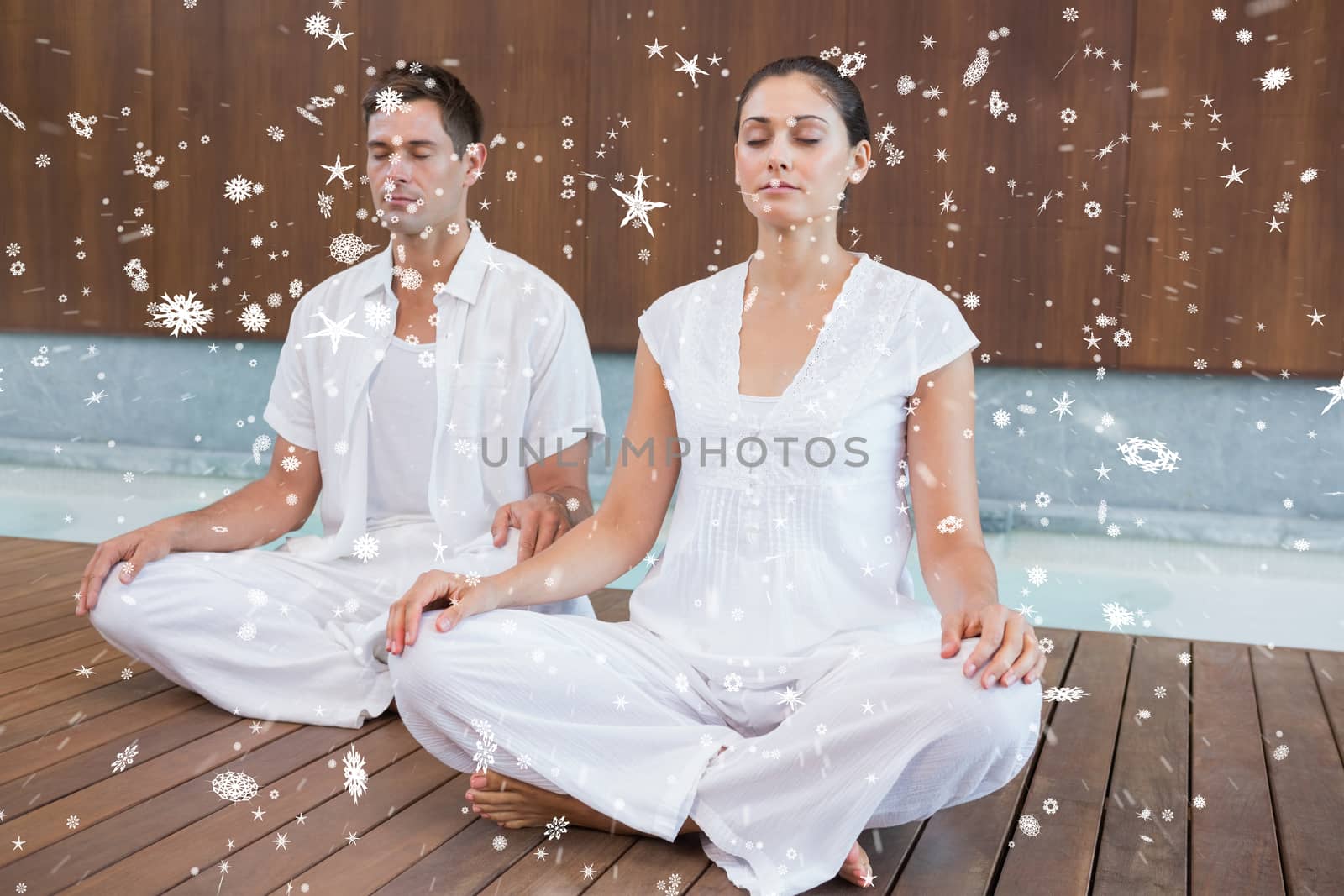 Attractive couple in white sitting in lotus pose against snow falling