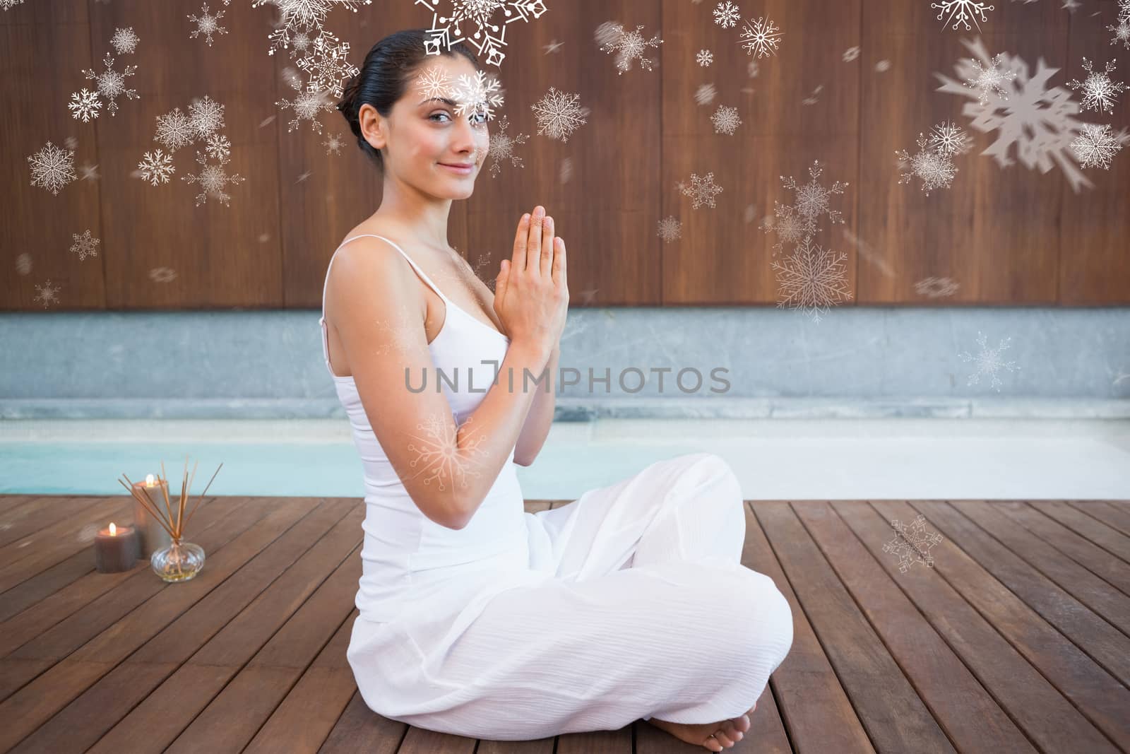 Content brunette in white sitting in lotus pose smiling at camera against snowflakes