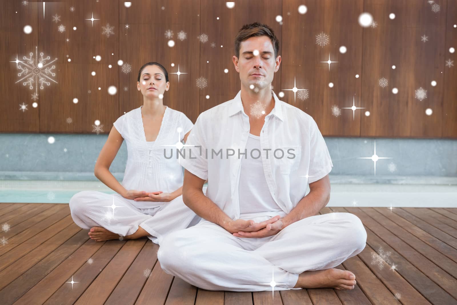 Peaceful couple in white sitting in lotus pose together against snow falling