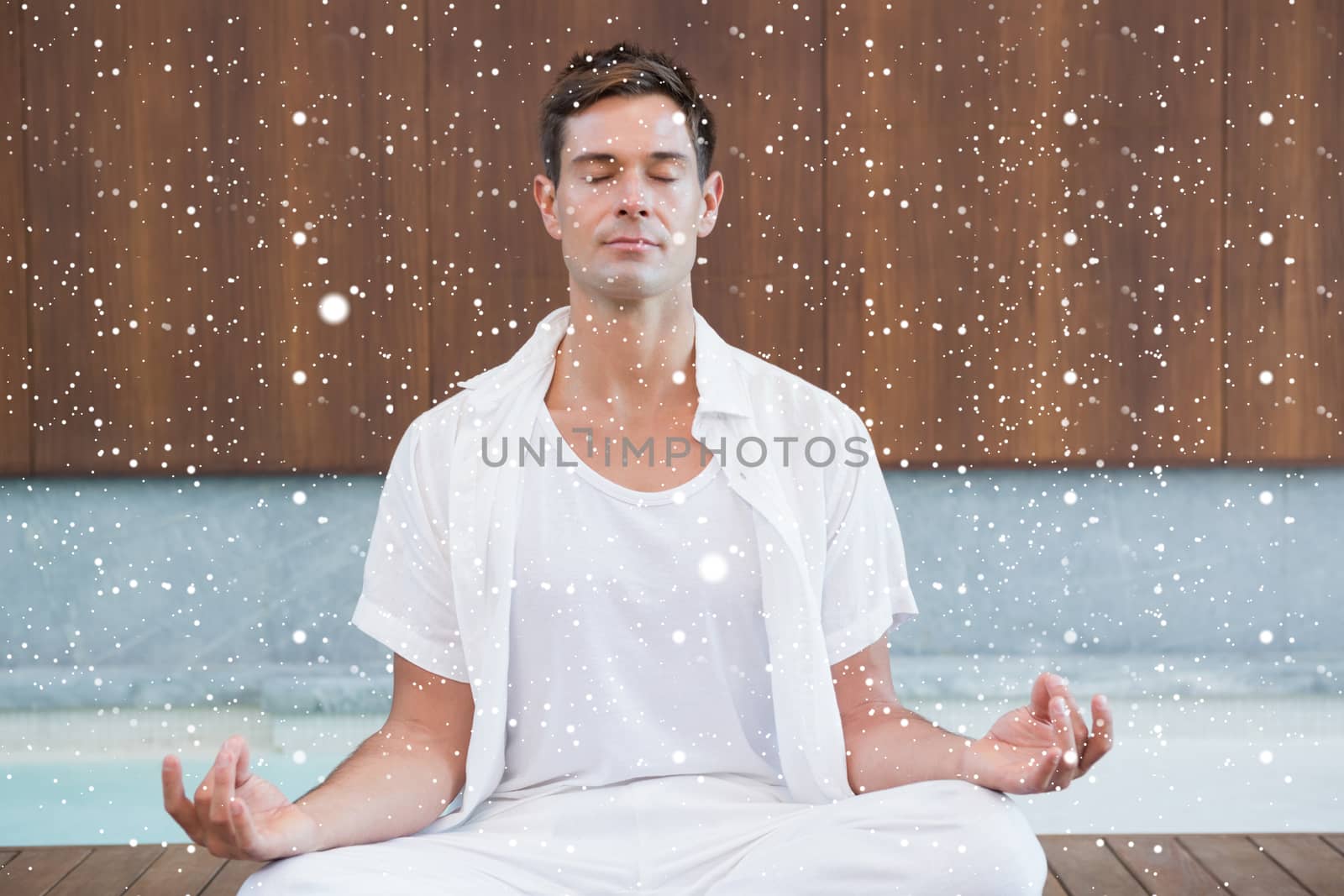 Handsome man in white meditating in lotus pose against snow falling