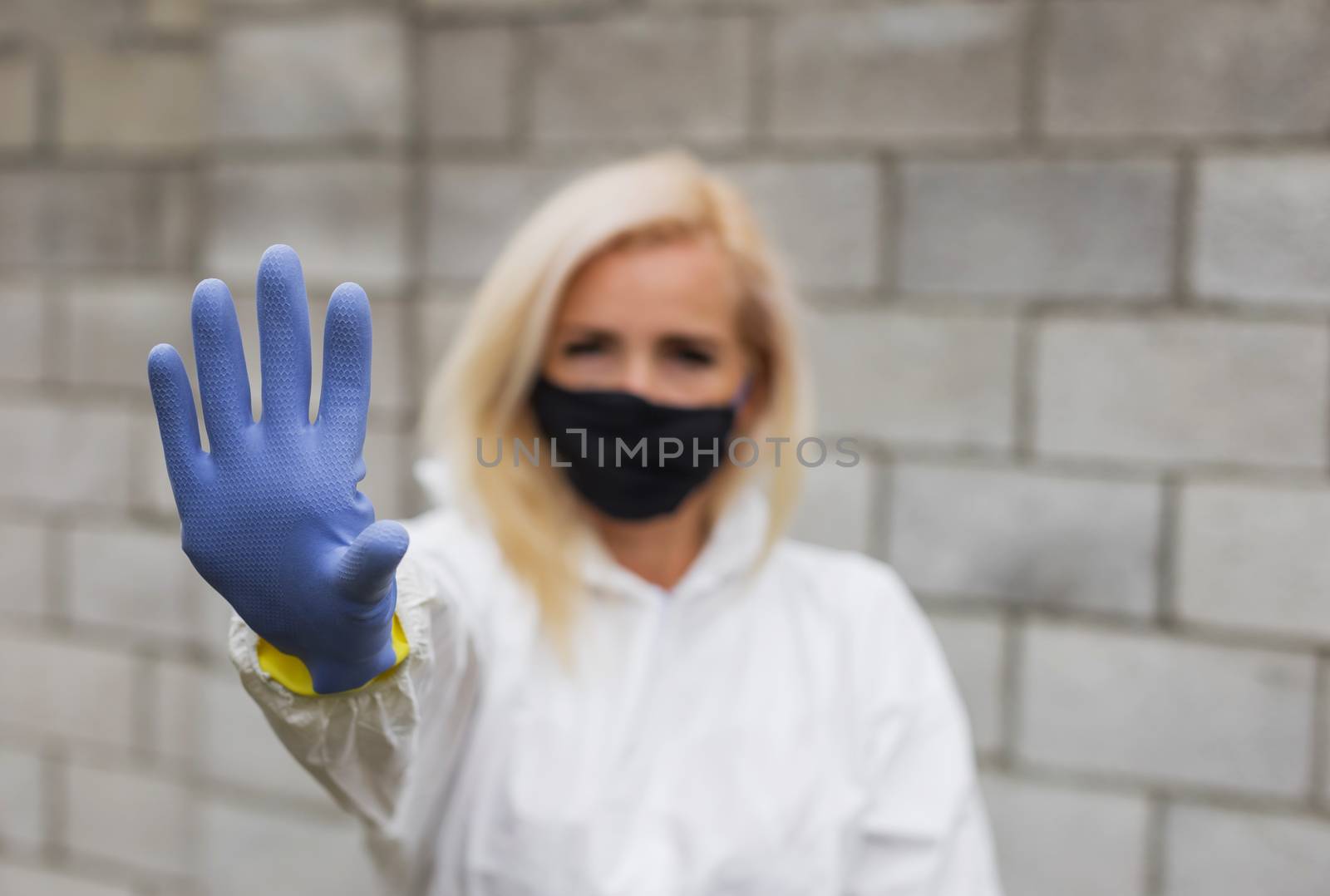 Woman in mask, white protective suit and gloves making sigh stop