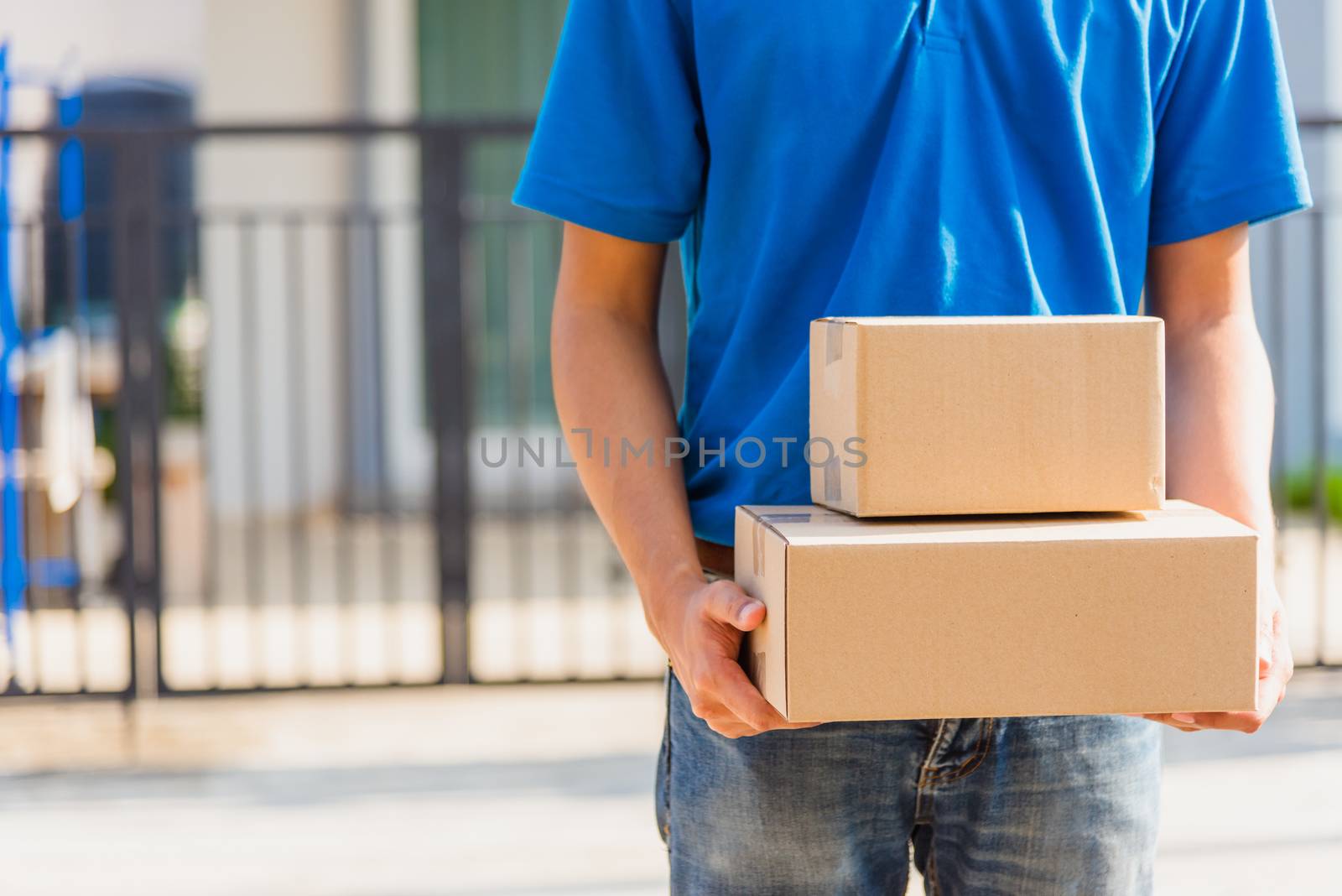 Asian Young delivery man courier online with box in blue cap and t-shirt uniform he protective face mask, service customer in front of the house under curfew quarantine pandemic coronavirus COVID-19