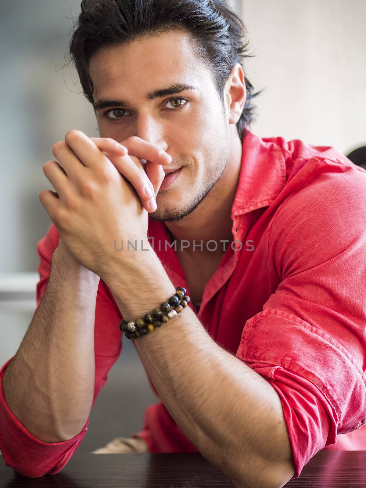 Attractive young man indoors wearing a shirt and beaded bracelets