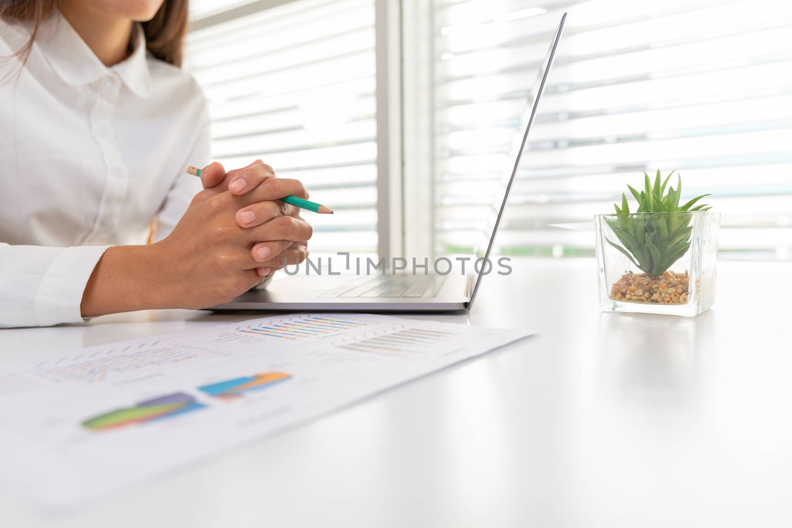 A business woman sitting on a desk with a laptop and graph with  by Kanjana
