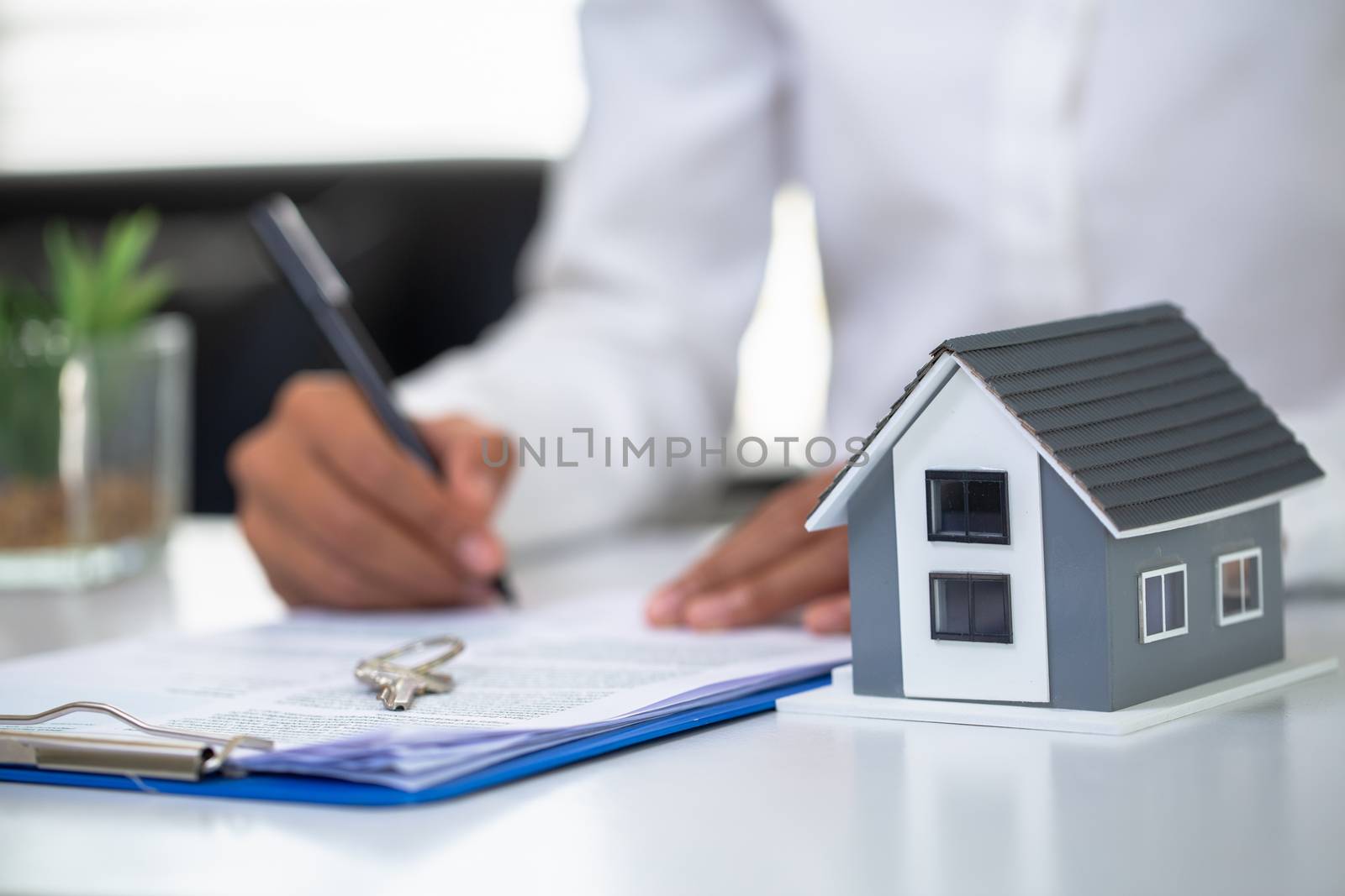 Businessmen and customers are signing home purchase agreements. Hand holding the pen signing purchase contract. Gray roof houses and keys placed close to each other.Real estate mortgage home purchase. by Kanjana