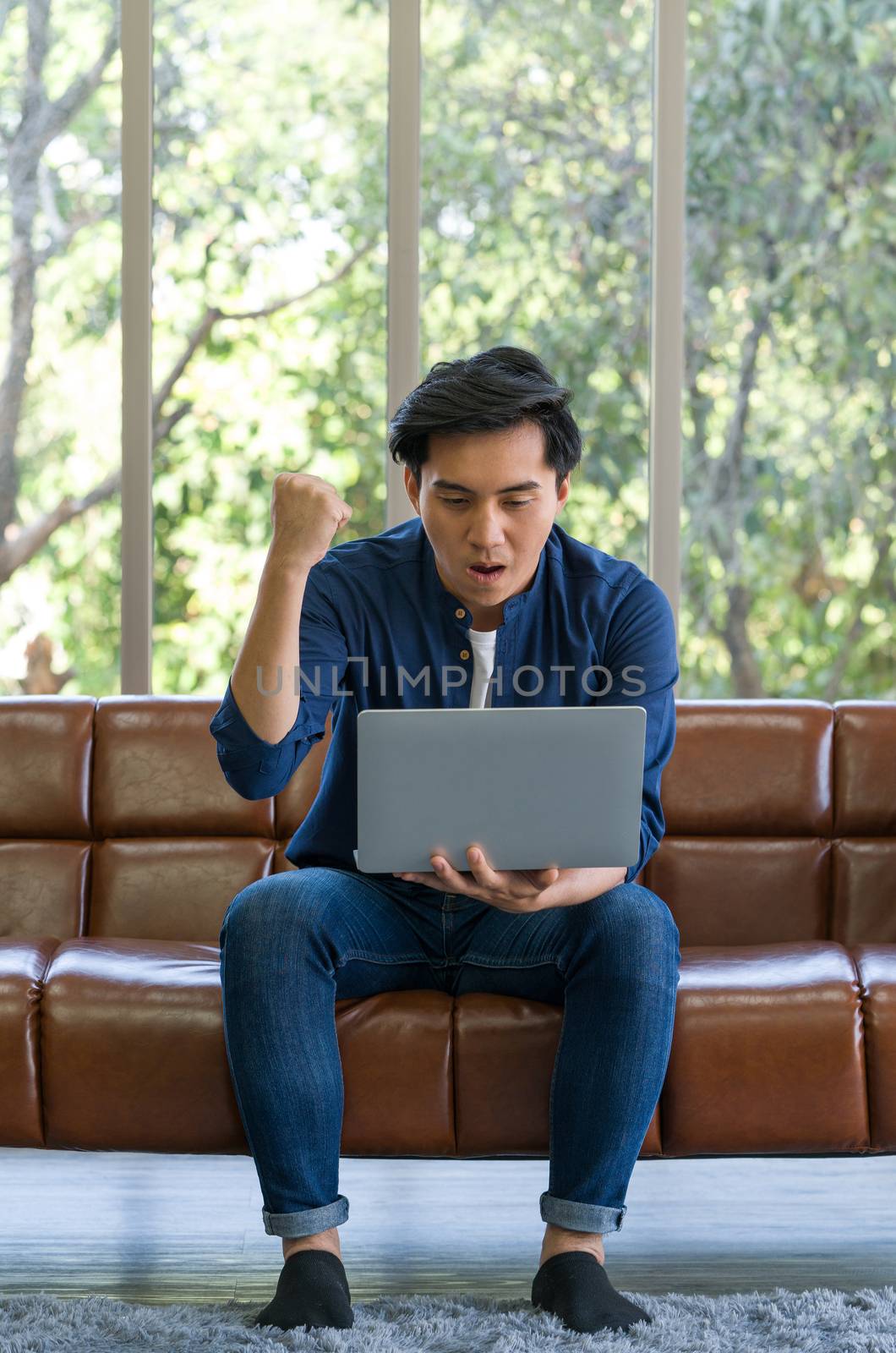 Asian man spend holidays in the living room. The young man wore comfortable clothes use laptop computer to search for jobs, and he got a job.