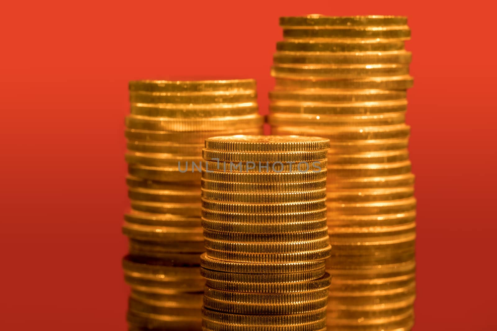 Focus on a stack of gold coins with other coin stacked in the background out of focus against red backdrop