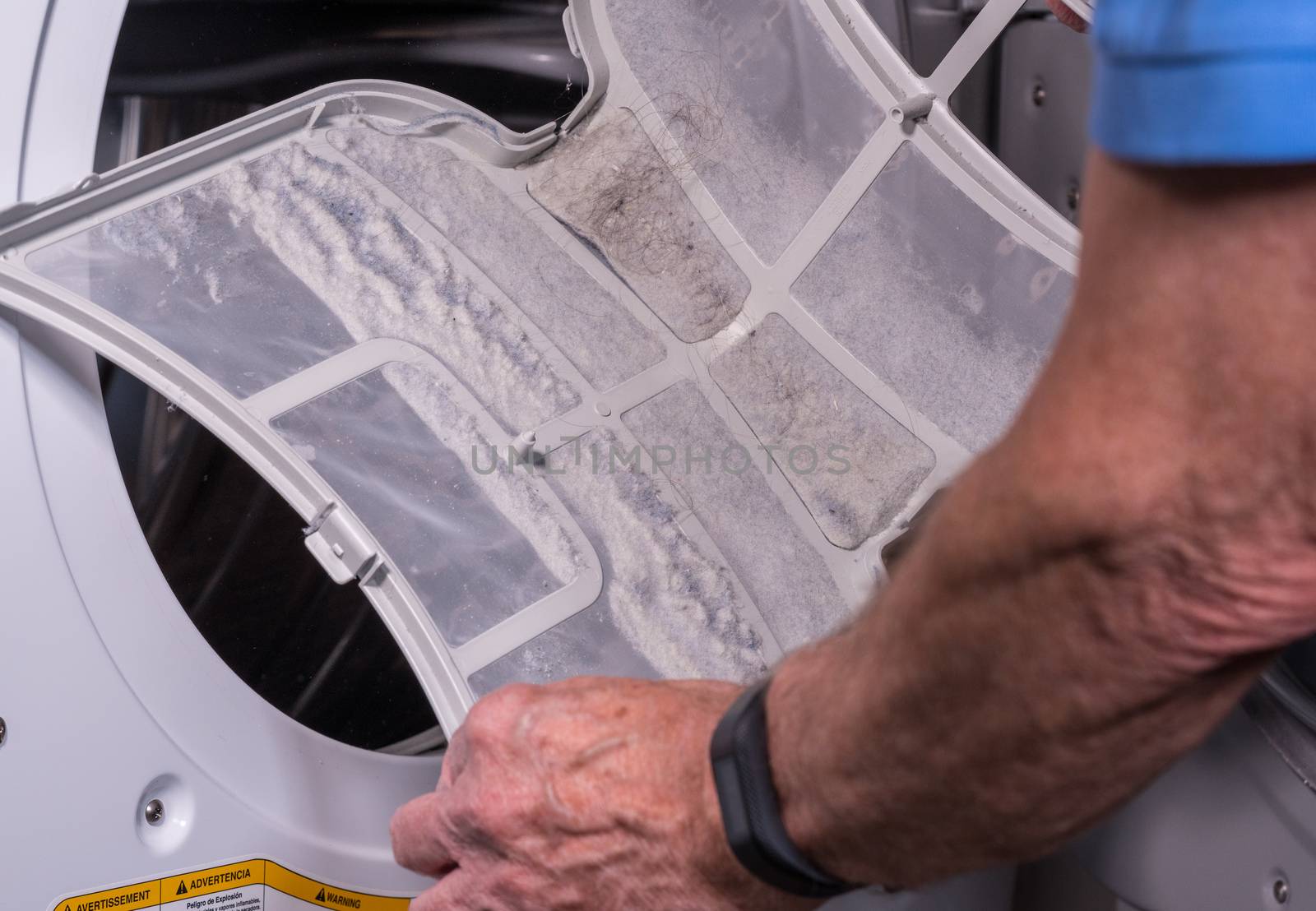 Senior caucasian man holding the lint filled trap from a front loading tumble dryer