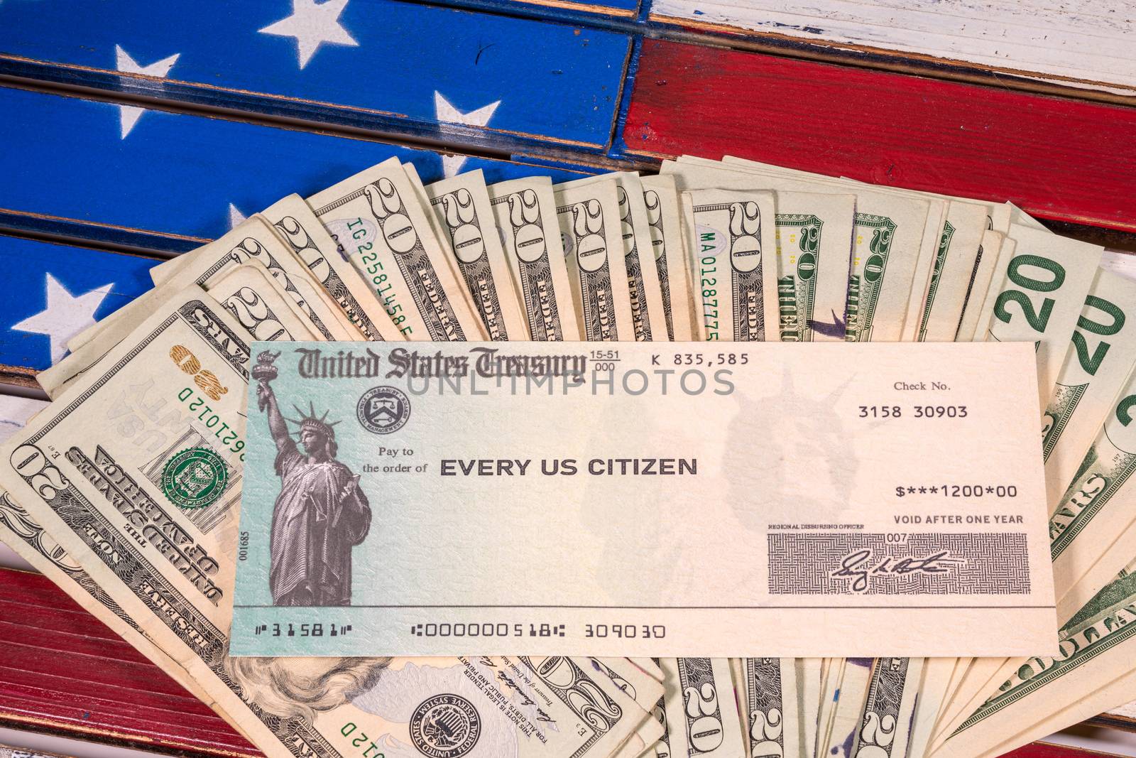 Stack of 20 dollar bills with illustrative coronavirus stimulus payment check on USA flag