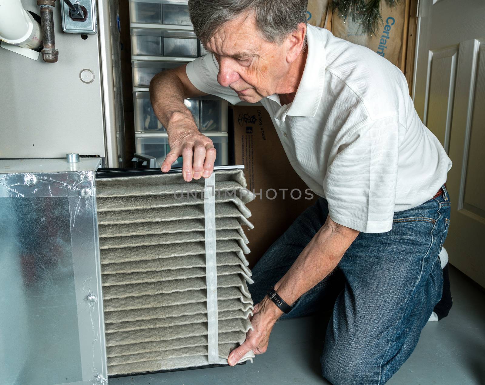 Senior caucasian man changing a folded dirty air filter in the HVAC furnace system in basement of home