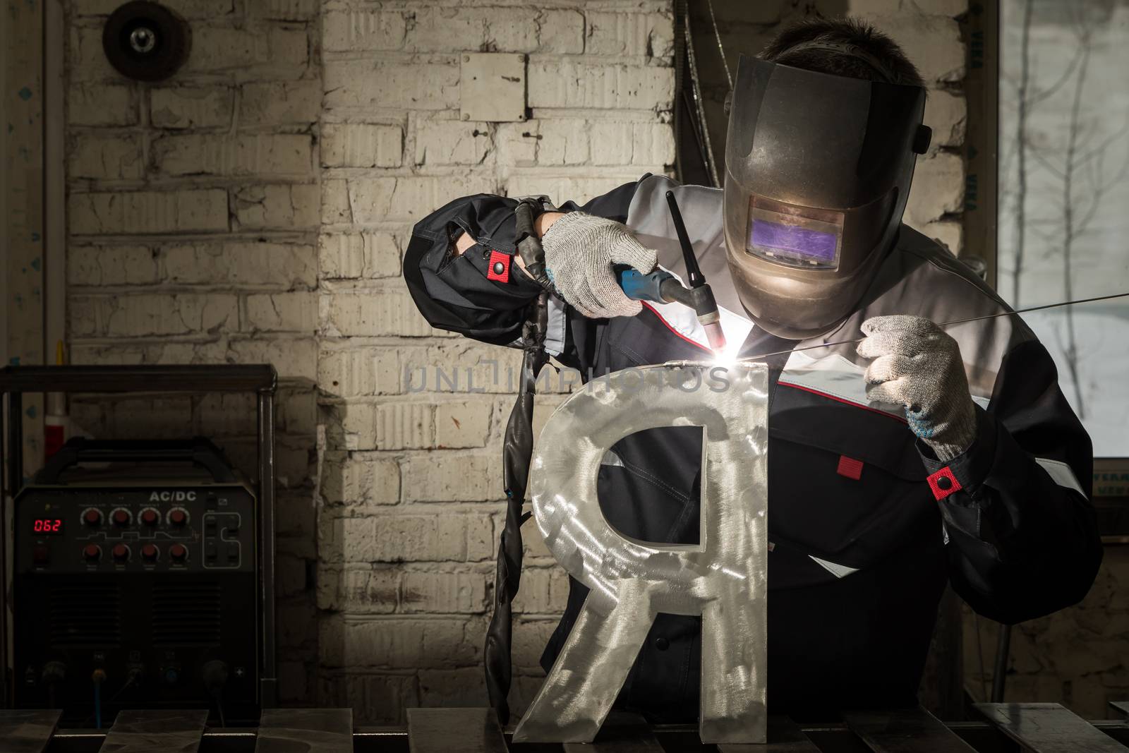 Welder welding a metal part in an industrial environment, wearing standard protection equipment. Sparks flying, fumes, industrial background