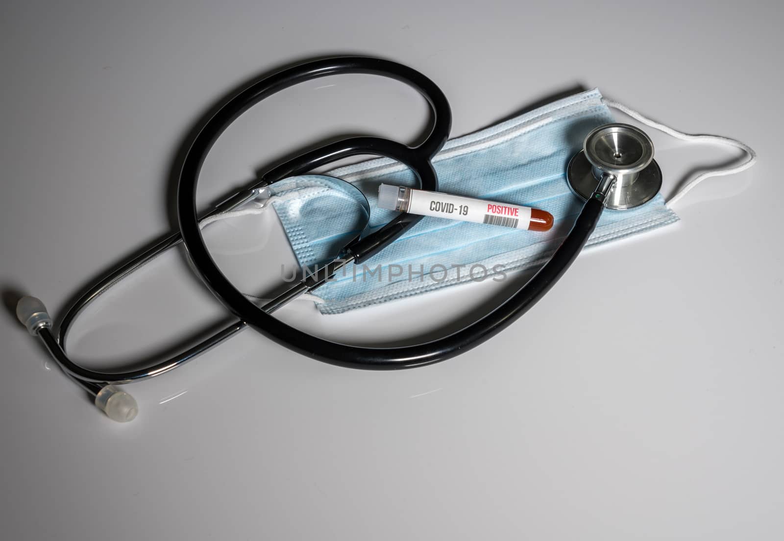 Positive blood test for Coronavirus laying on doctor surgical mask with stethoscope to show danger to front line medical workers