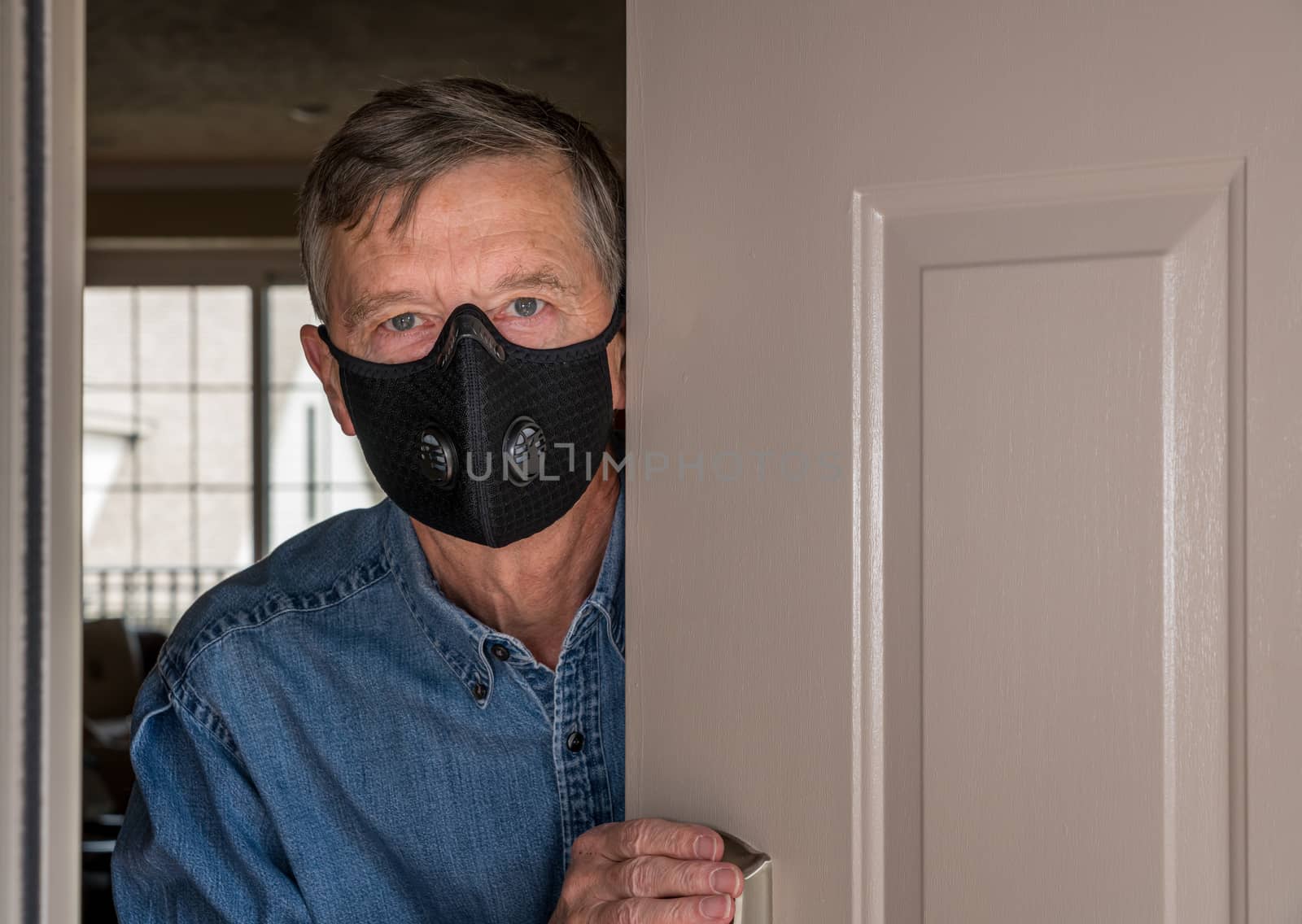 Senior man with face mask looking worried at front door in case visitors bring coronavirus to his home