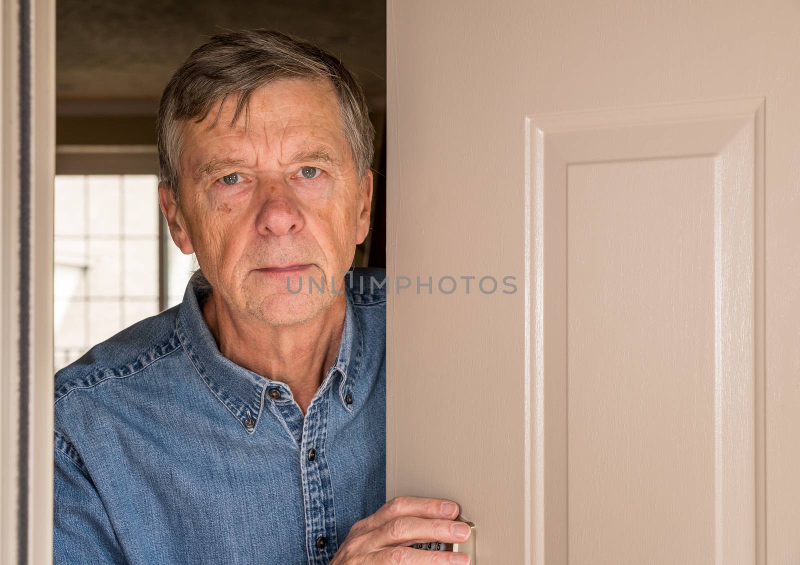 Senior man with looking worried at front door in case visitors bring coronavirus to his home