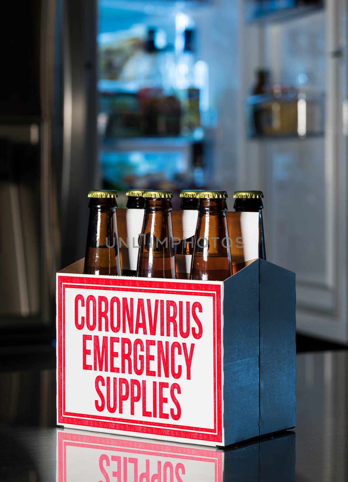 Six pack of brown beer bottles in box with Coronavirus Emergency Supplies stamped on side. Cold fridge out of focus in rear. Humorous view of hoarding