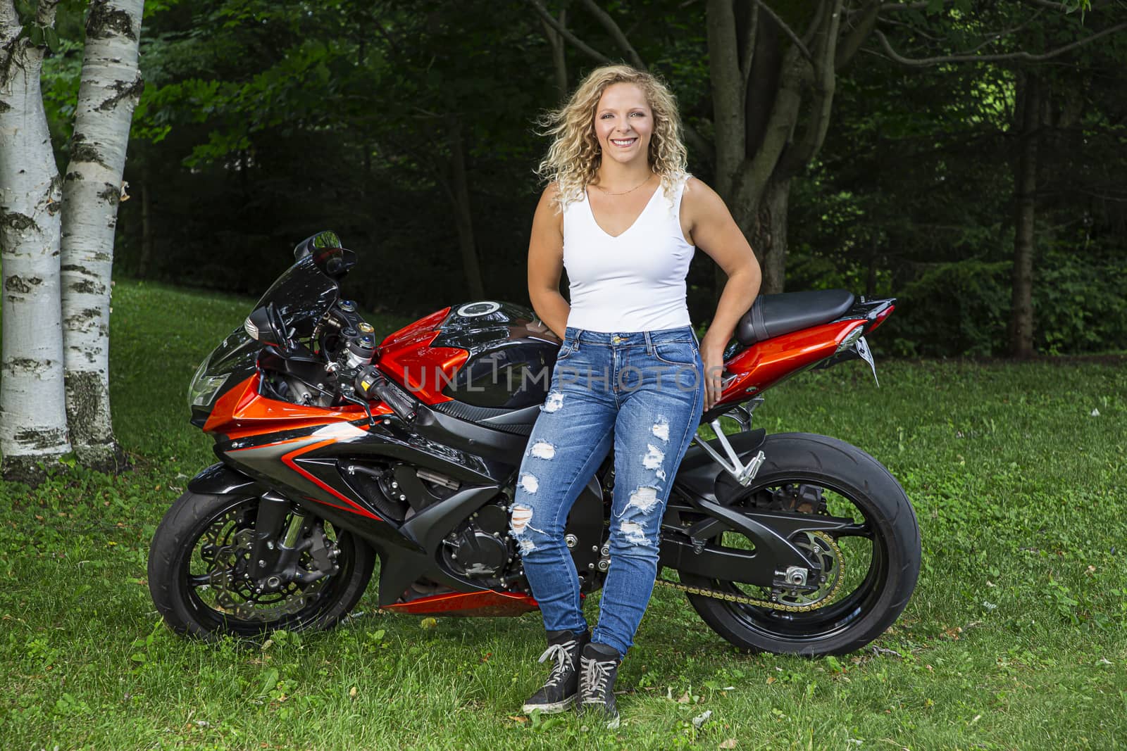 twenty something blond woman leaning against a sport motocycle in a park