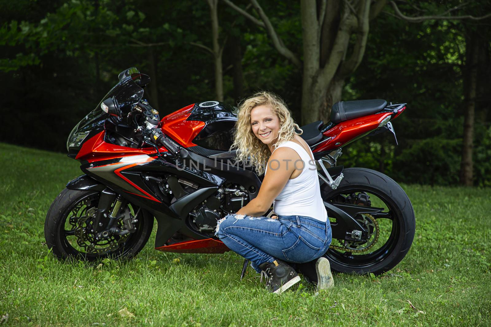 young woman leaning close to a sport motocycle in a park