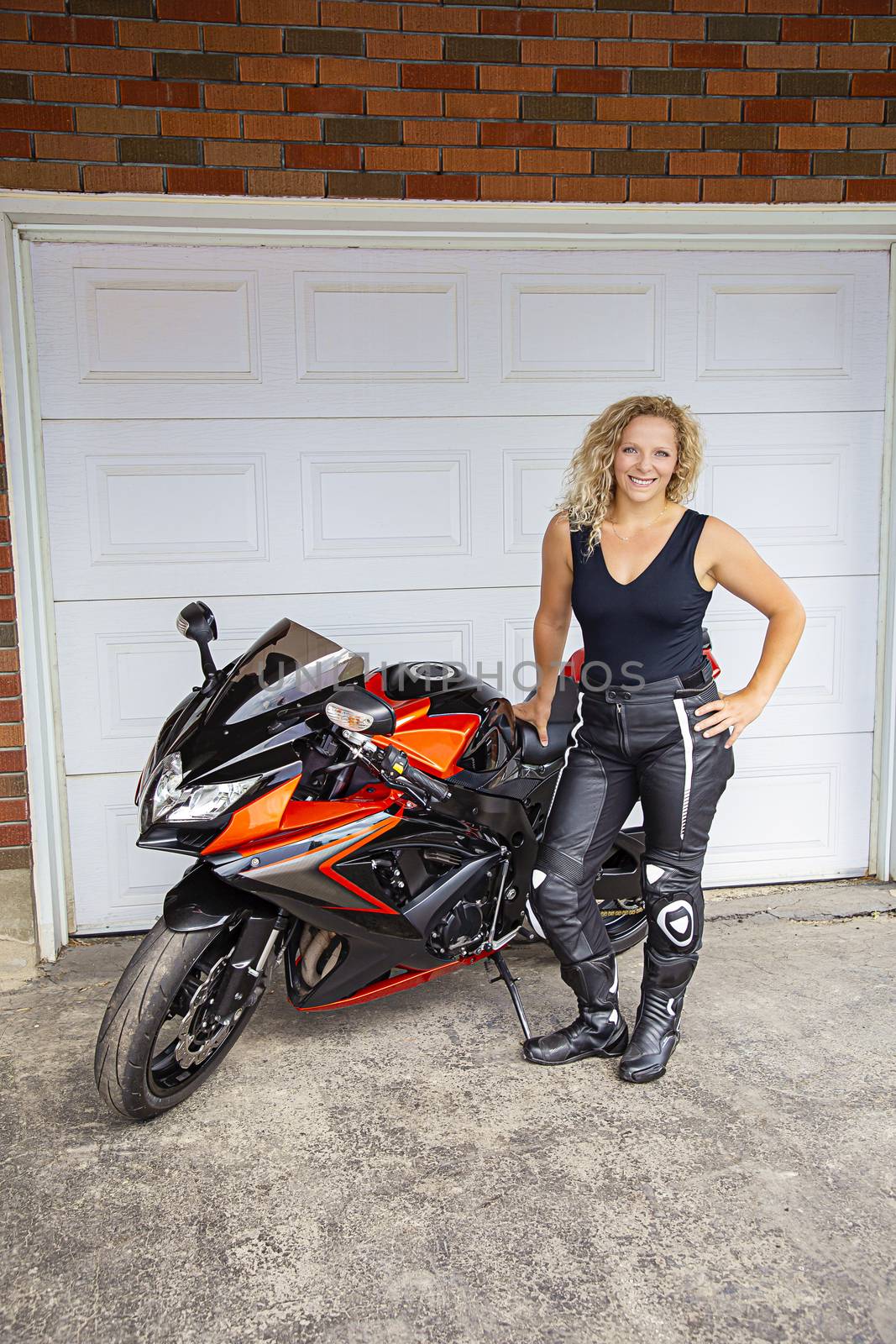 young woman standing beside her motocycle, in front of a garage door