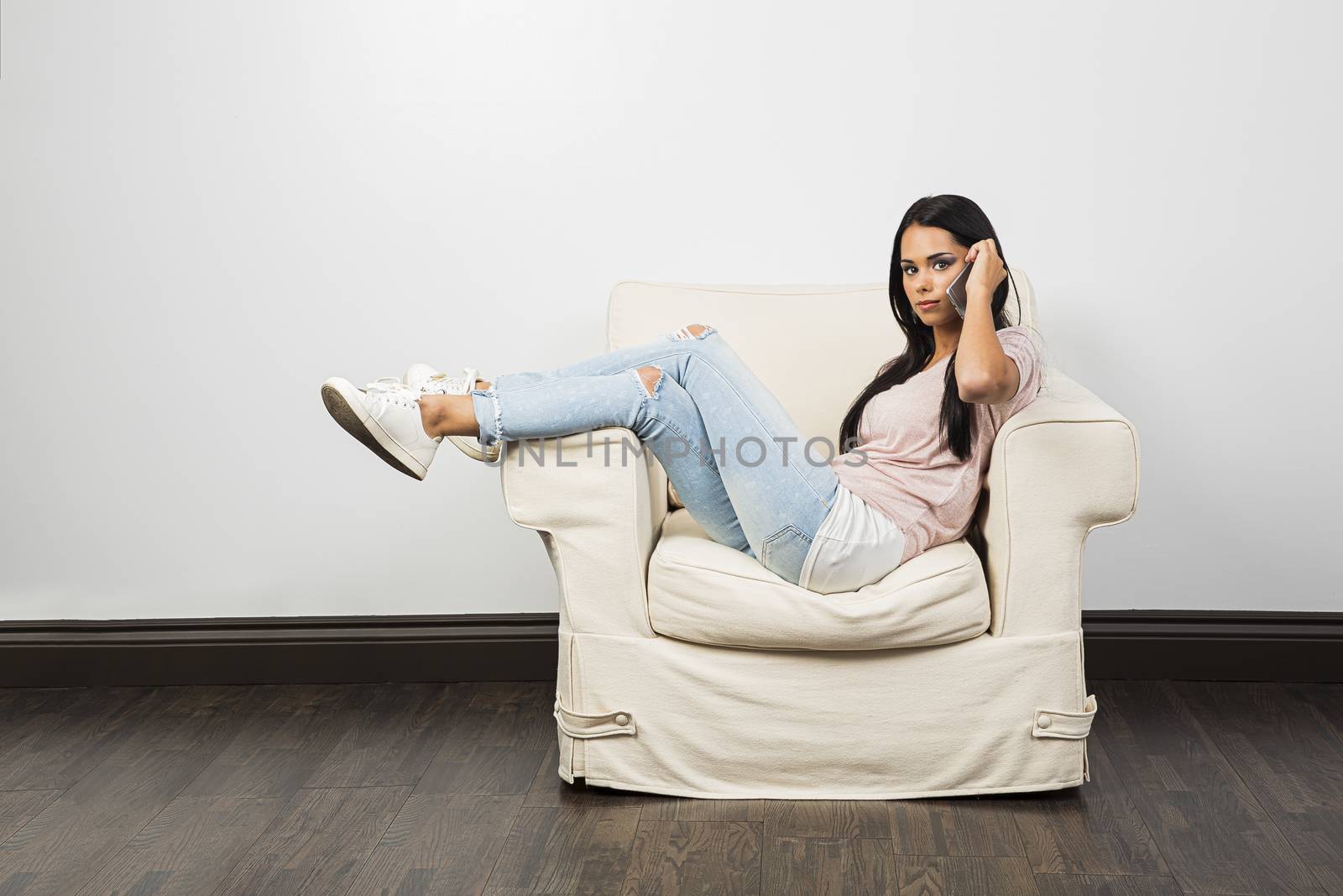 Young woman, with her legs up on a white couch, talking on a phone