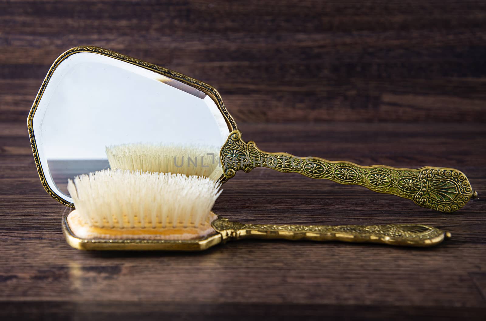 antique hand mirror and hair brush against a dark wood background