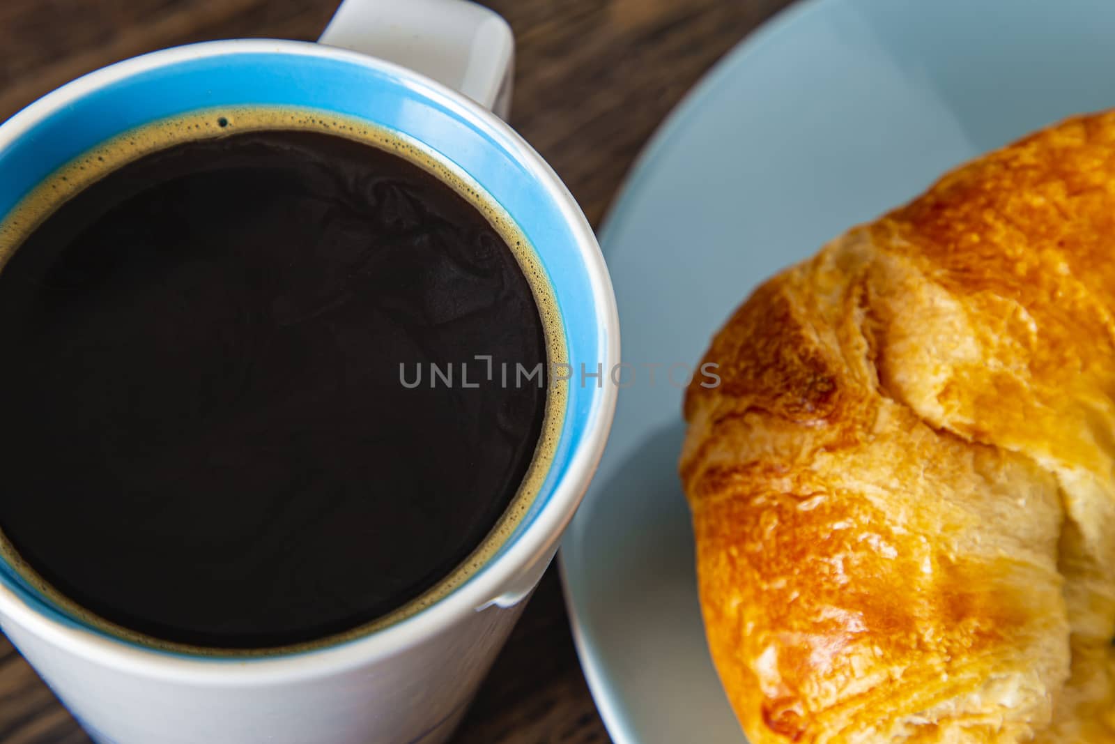 Close up of a coffee cup and a croissant on a blue plate