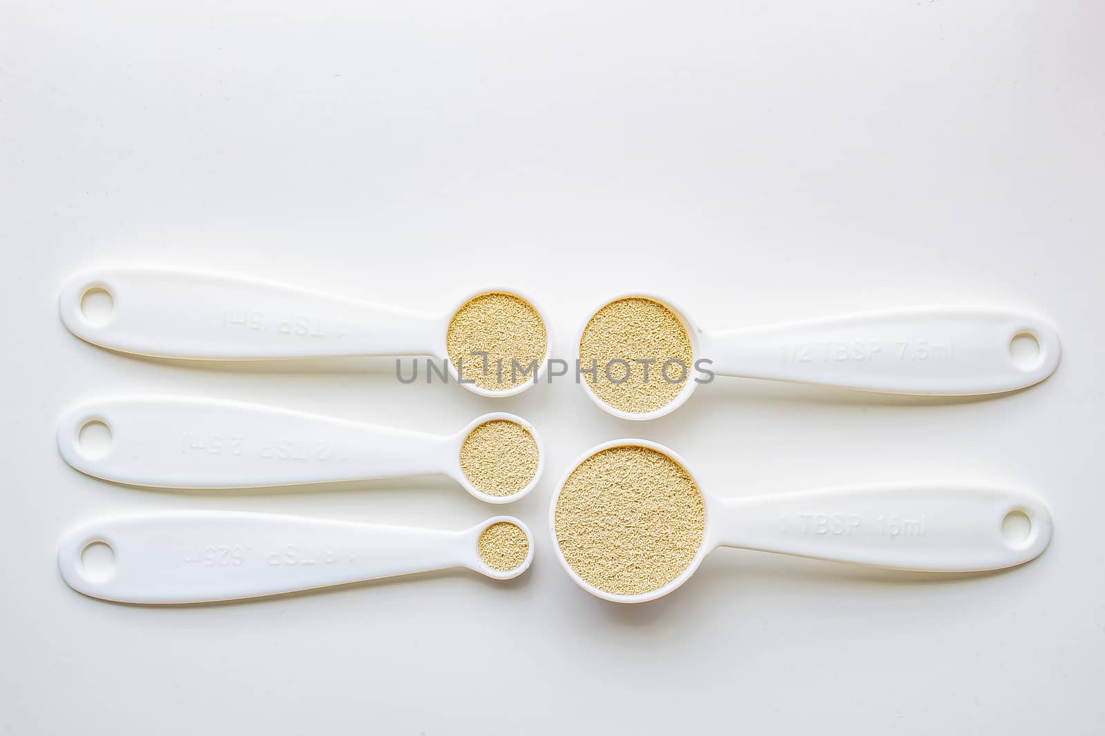 A top general view of some measurement baking spoons with yeast on them