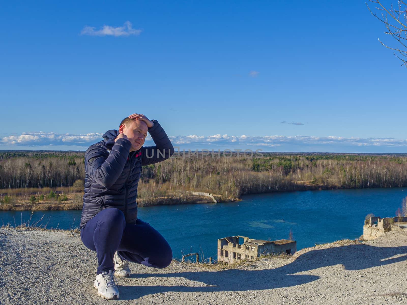 Man sitting on the pick of a mountain and looking into the distancee. Vantage point of Rummu quarry, Estonia. Clear blue sky. Travel concept. copy space