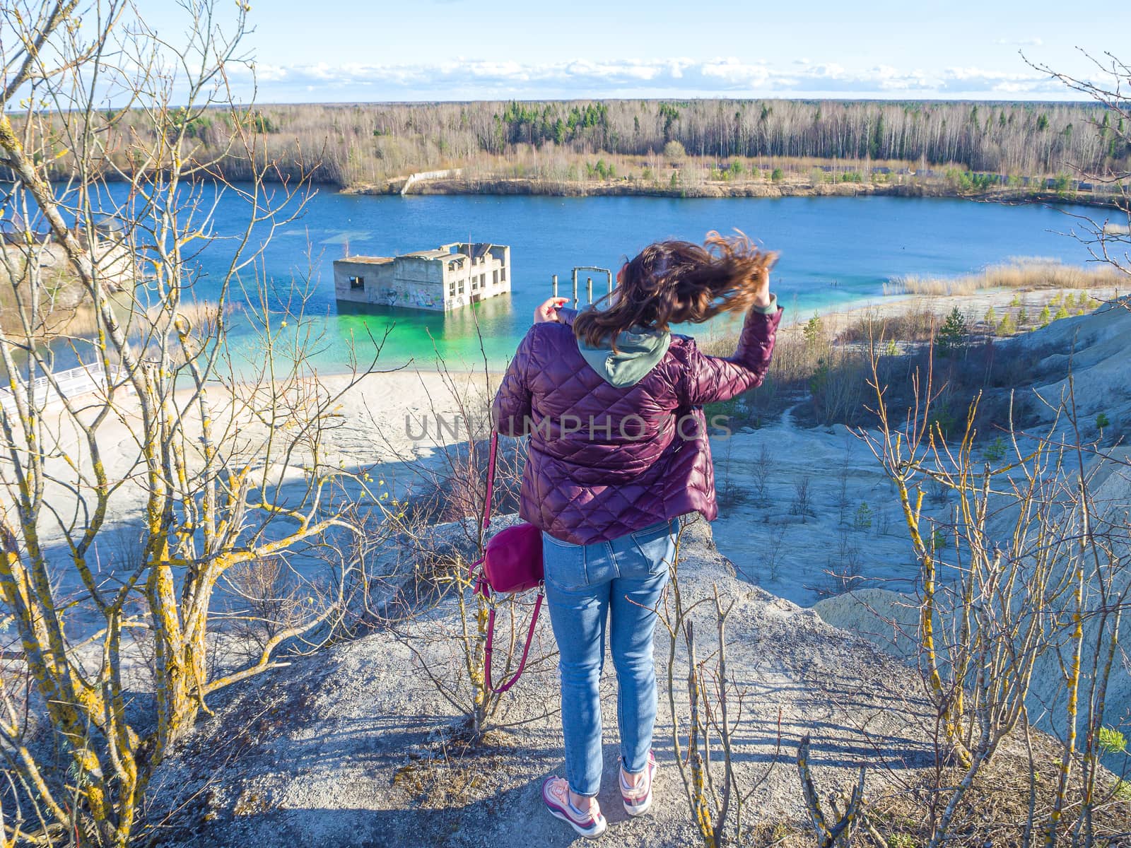 Hiker on mountain top. Woman is standing with an Abandoned Quarry and water on the background. Scenic View Of Land Against Clear Blue Sky. Panoramic View.