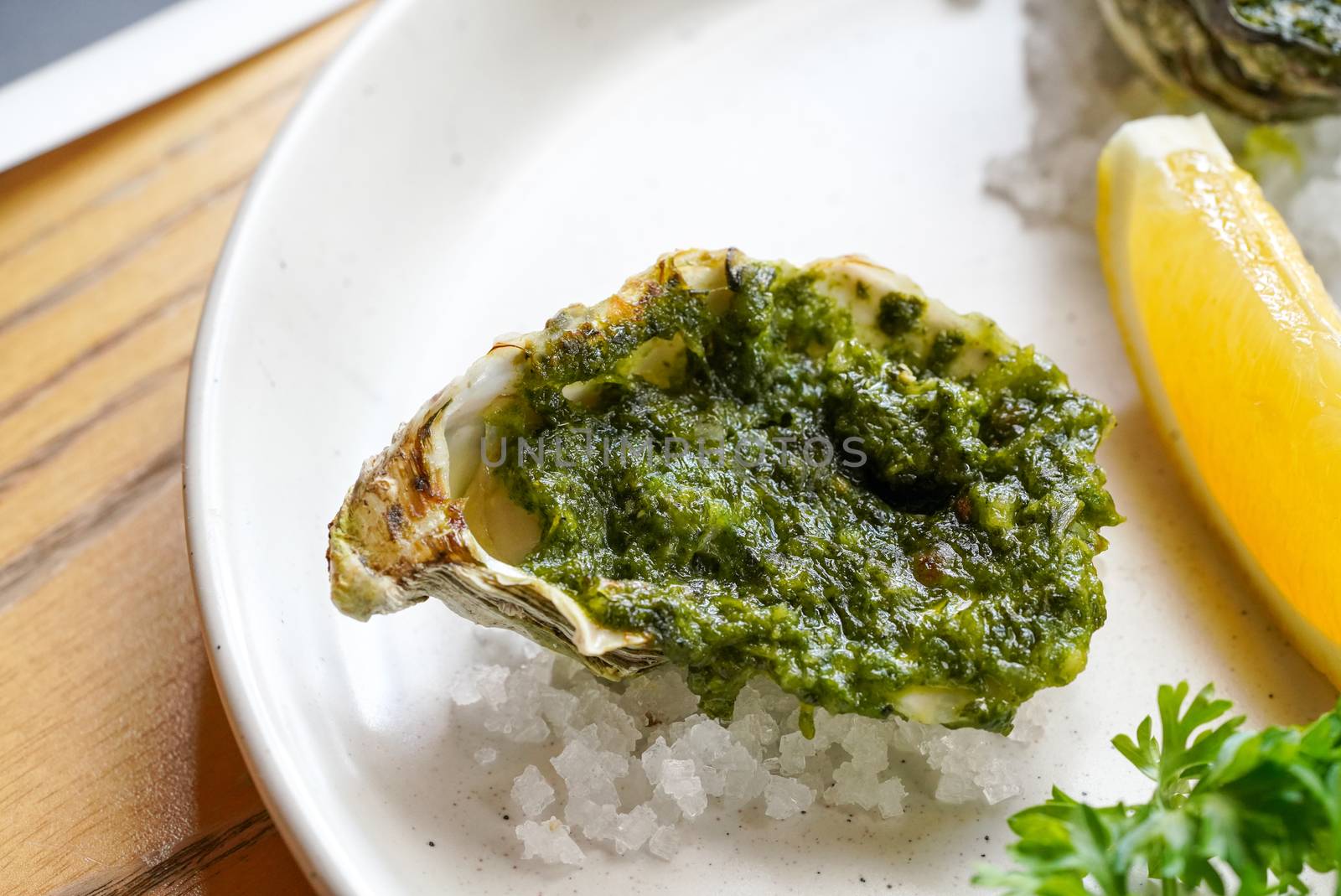 Half-shell oysters  topped with a rich sauce of butter, parsley and green herbs served on white plate by chadchai_k