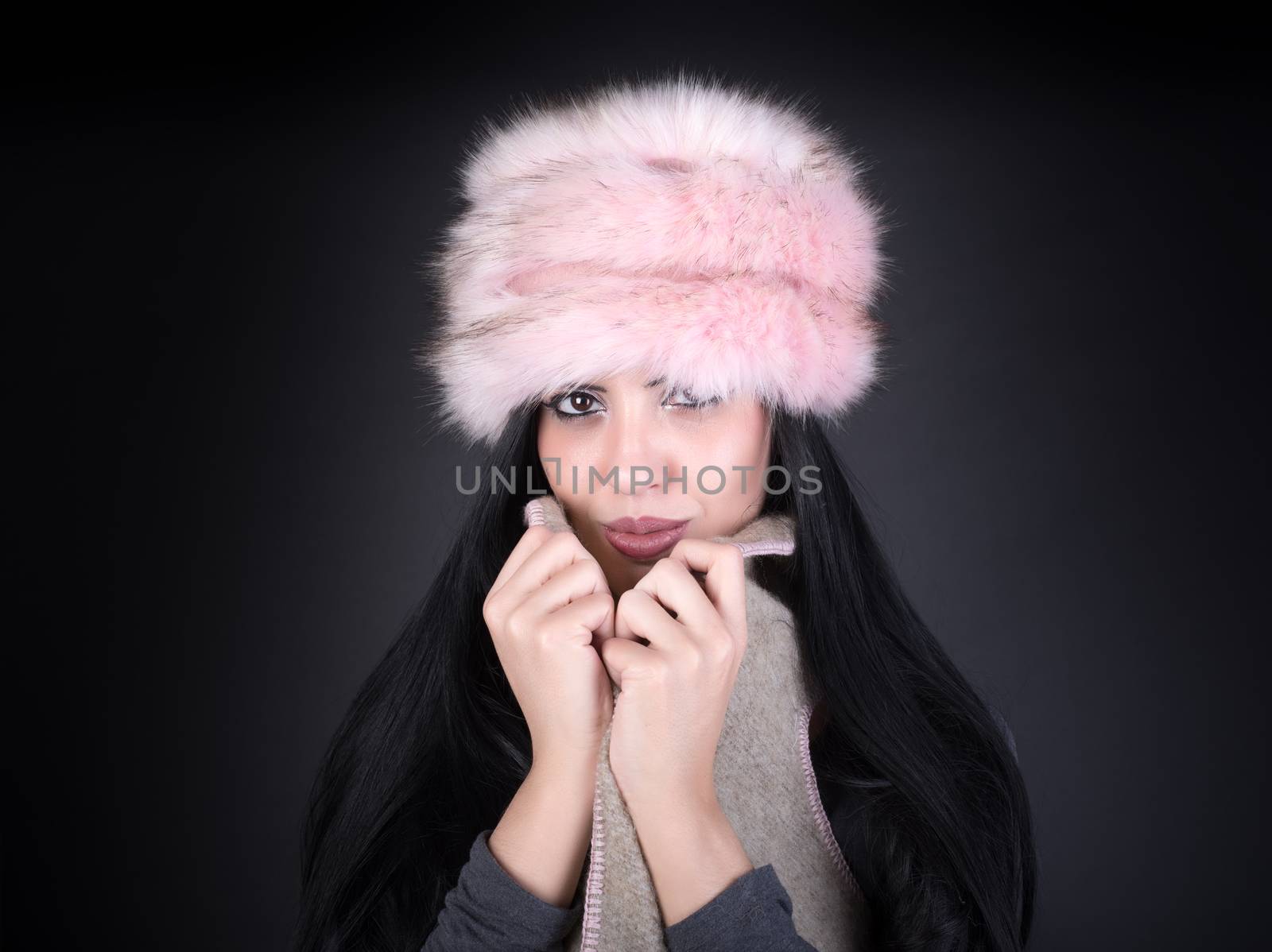 Winter portrait of a young woman in a pink hat on black background