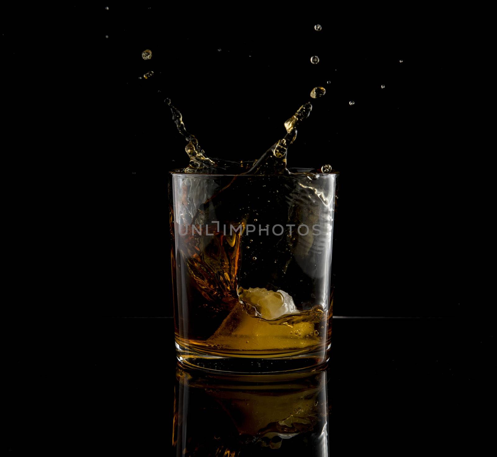 Splash in glass of whiskey and ice block falling on black background