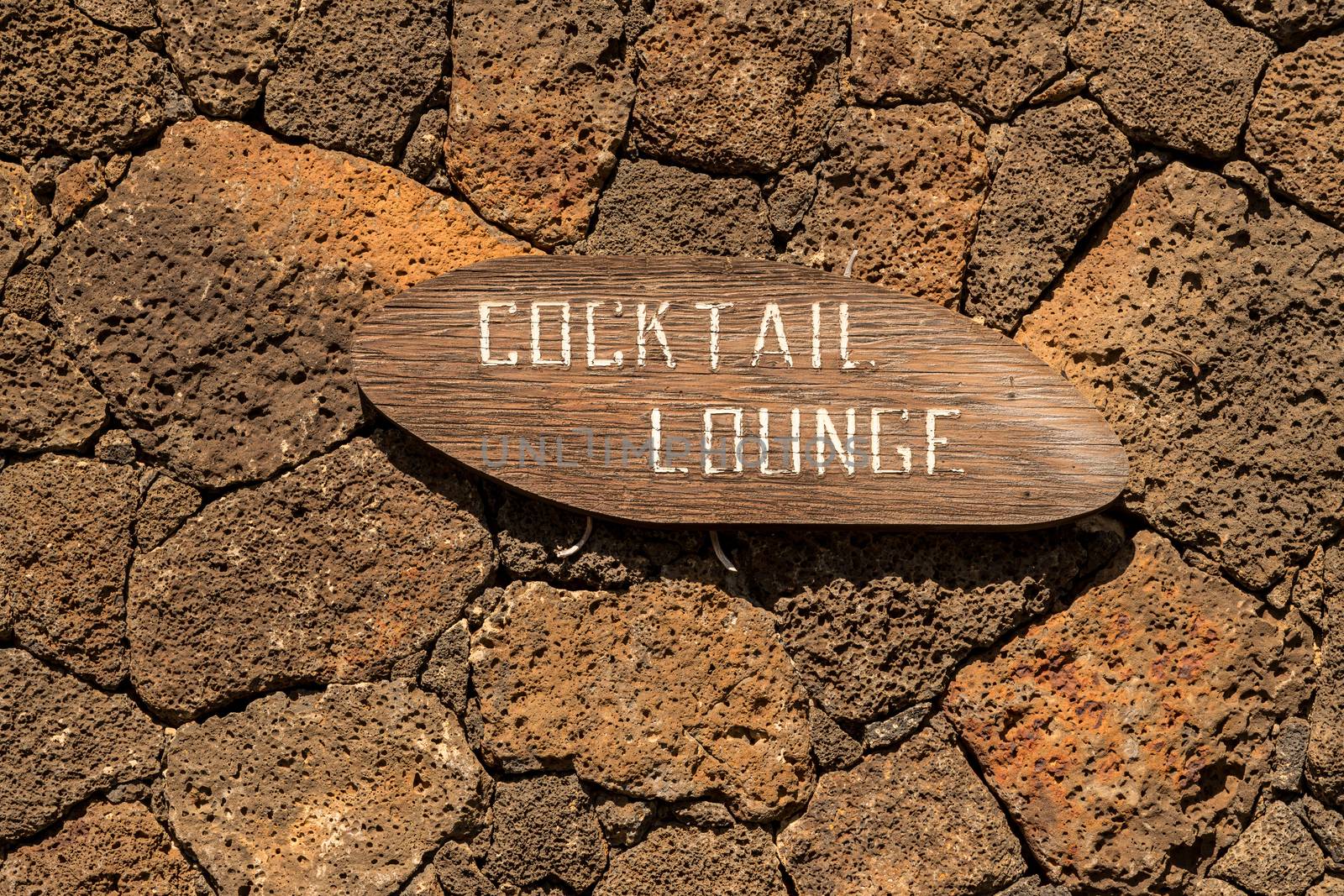 Cocktail Lounge painted on wooded sign fixed to lava rock wall and looking very faded and old fashioned