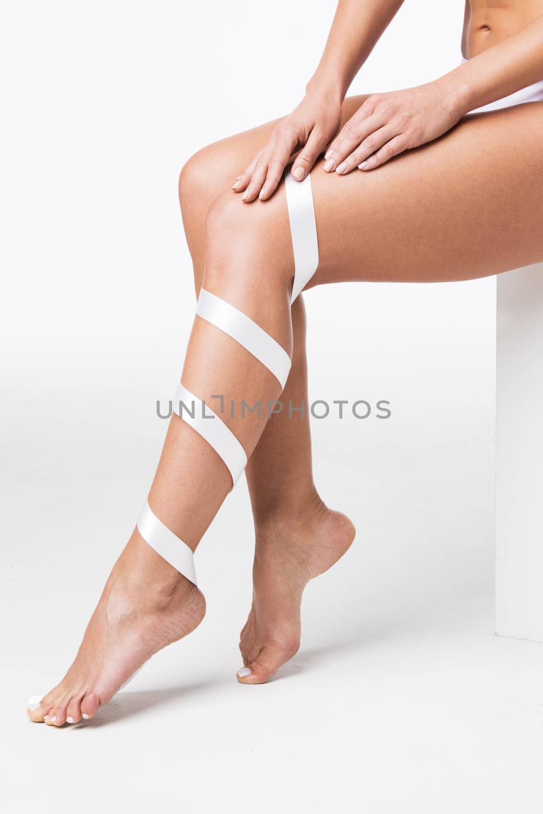 Closeup of perfect women's legs with white ribbon on white background