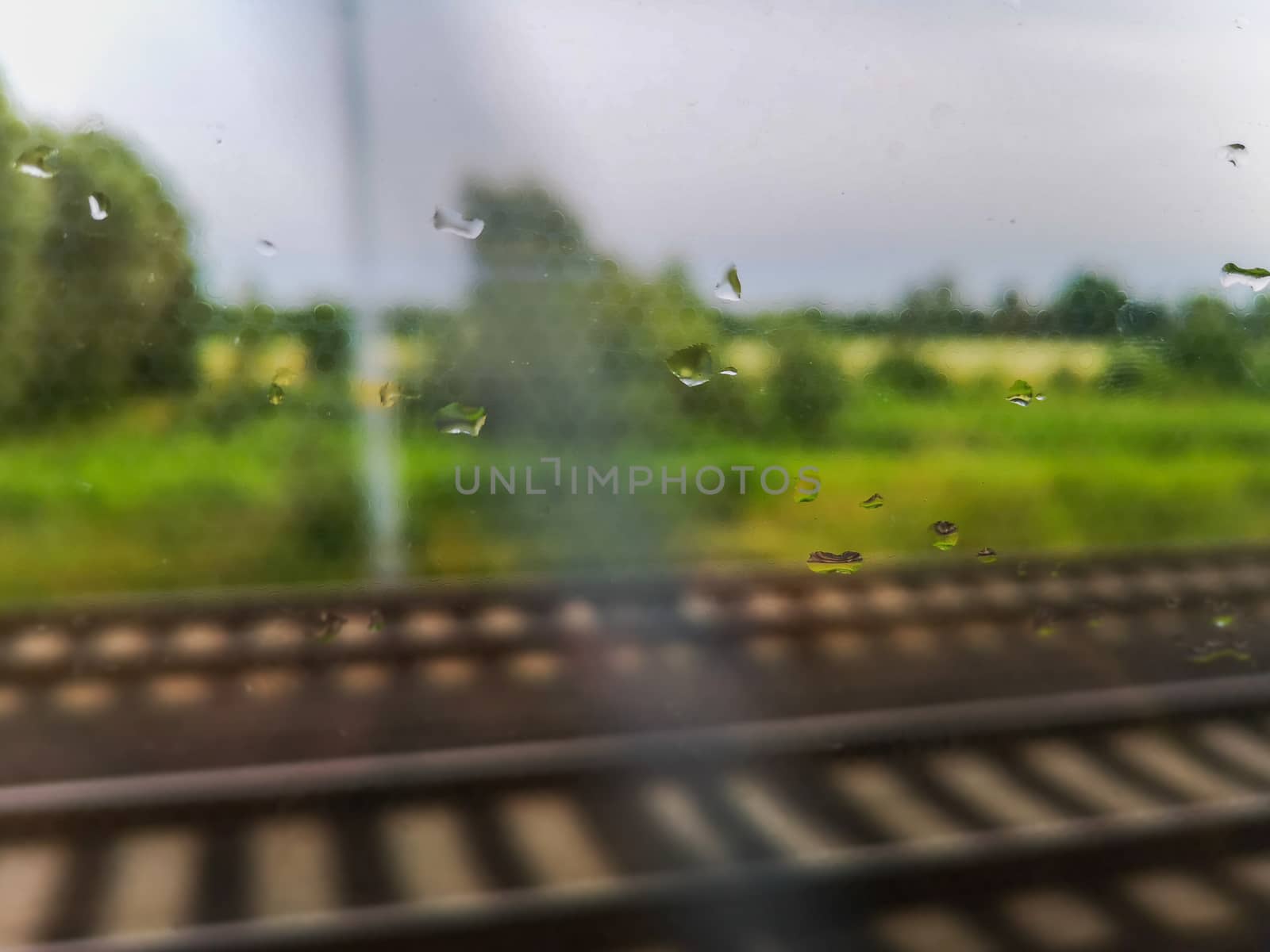 Rainy drops on train window at travel with rails and landscape behind window by Wierzchu