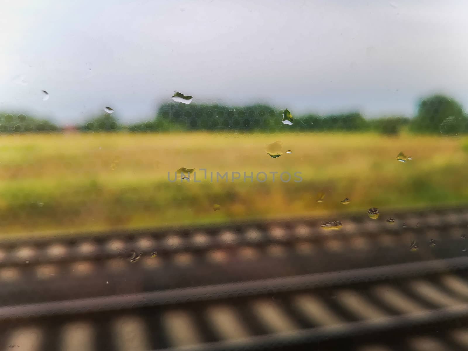 Rainy drops on train window at travel with rails and landscape behind window