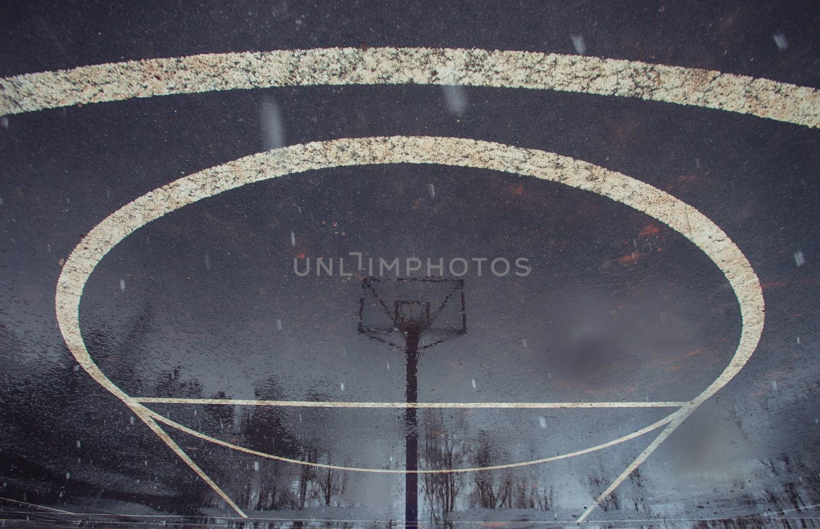 Basketball court after rain. Basketball half-court line. Outdoor court wet with rain. Court with reflective water. Tree and sun reflection on water. Abstract art. Minimal design. Abstract design