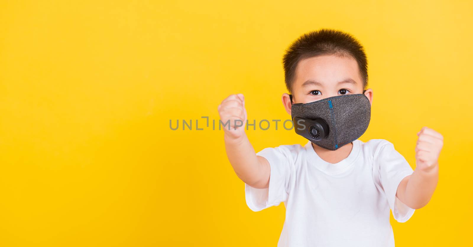 Asian Thai happy portrait cute little cheerful child boy wearing mask protective for covid-19 or pm2.5 dust he raise hands glad excited cheerful after recovering from illness, on yellow background