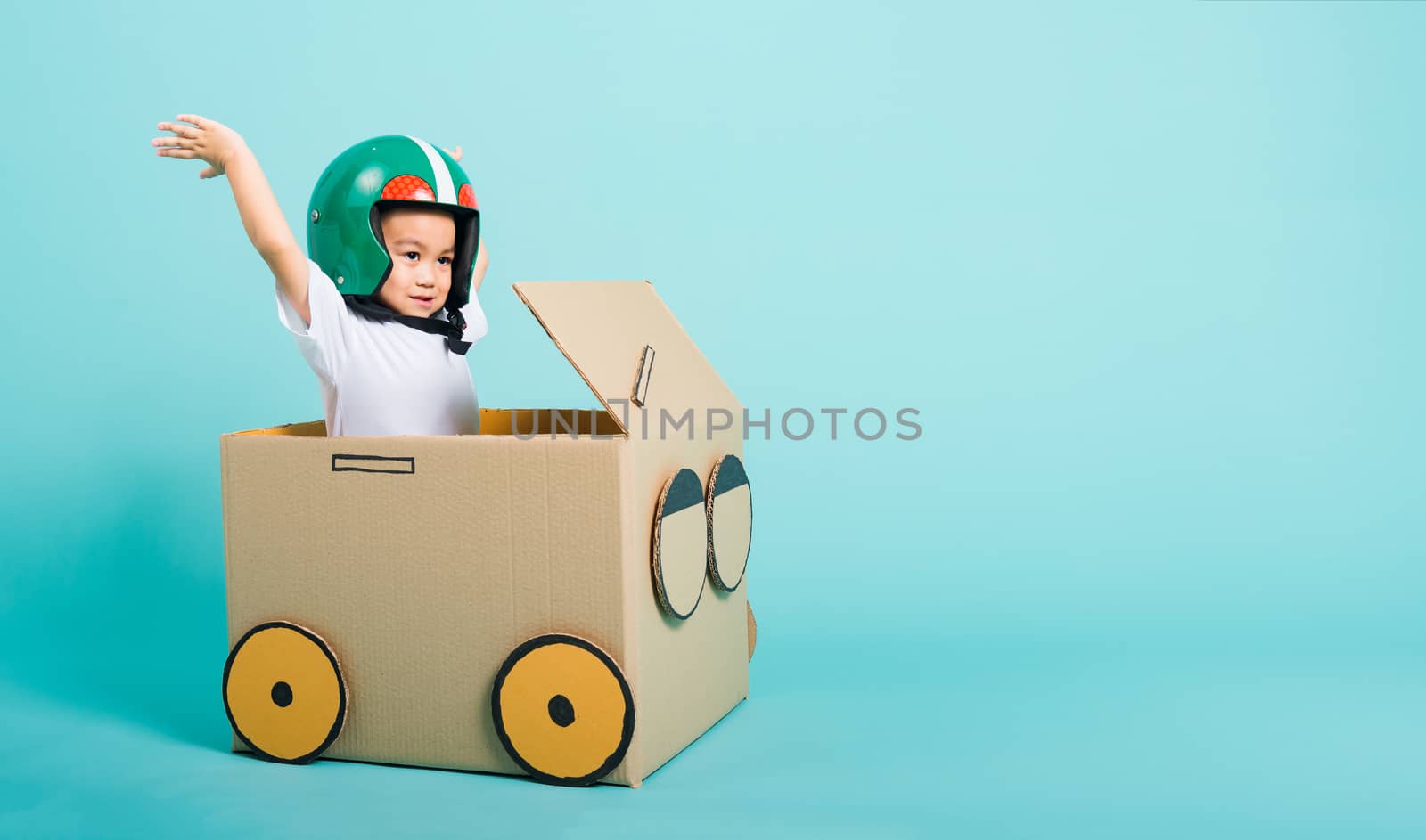 Happy Asian children boy with Helmet smile in driving play car creative by a cardboard box imagination, summer holiday travel concept, studio shot on blue background with copy space for text