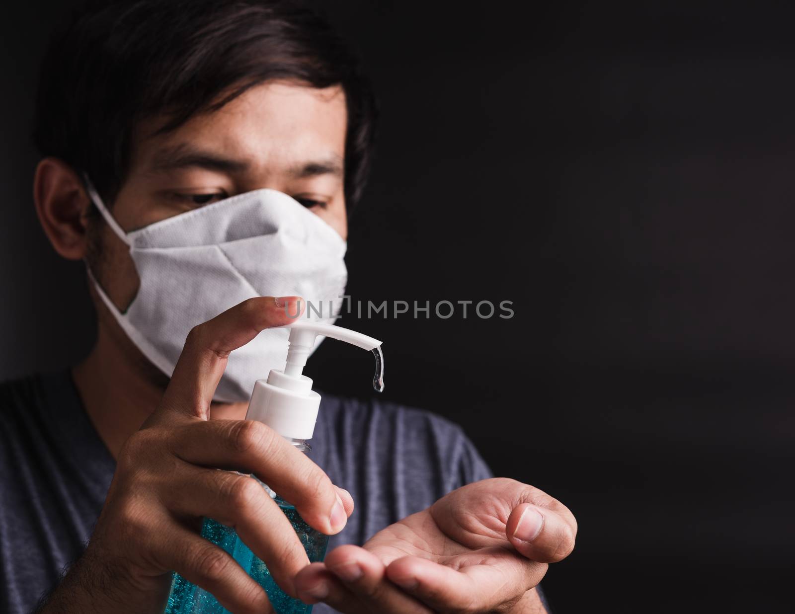 Closeup Asian handsome man wearing protective face mask fear in eye holding show sanitizer gel near face, hygiene prevention COVID-19 virus or coronavirus protection concept dark on black background