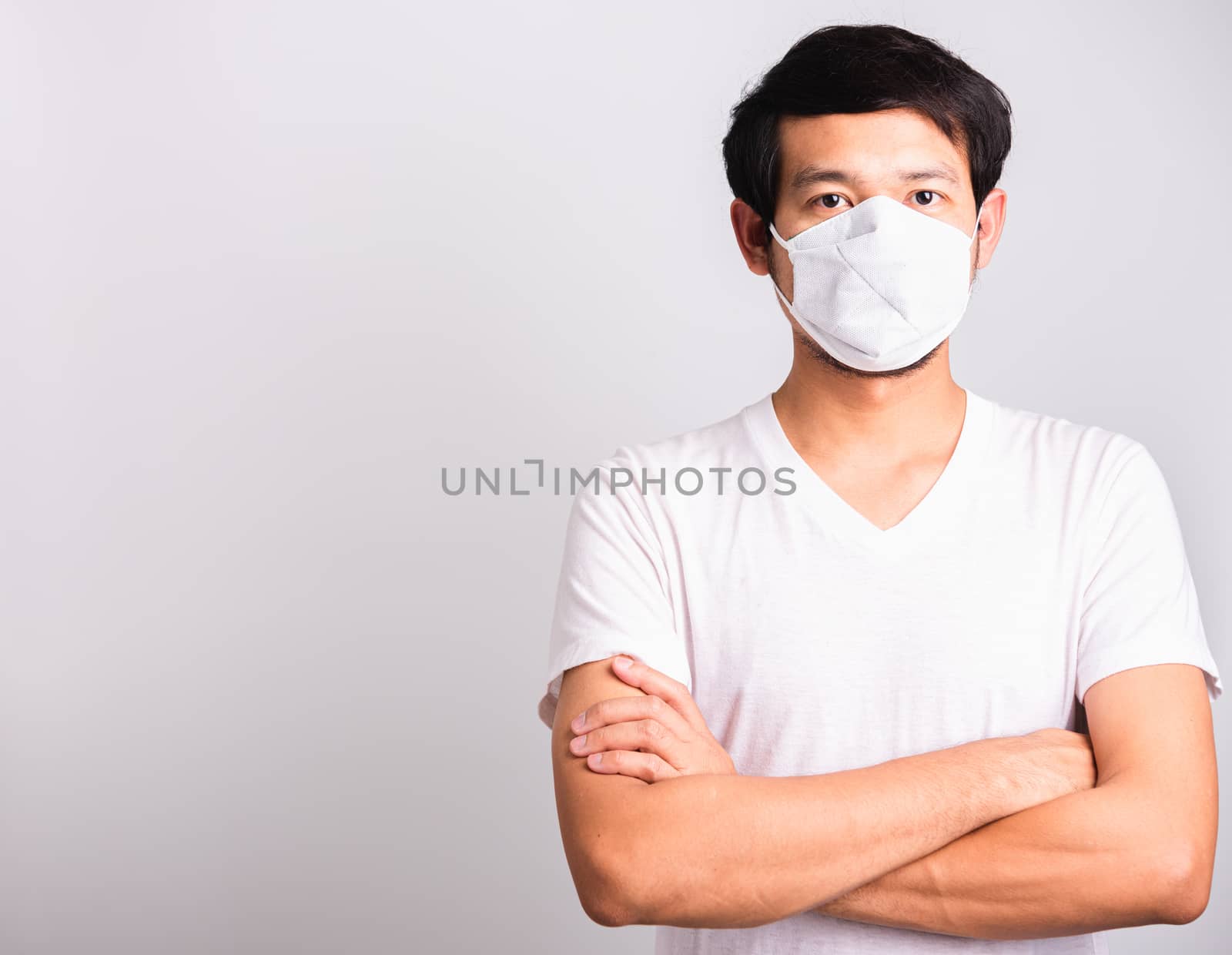 Closeup Asian handsome Man wearing surgical hygienic protective cloth face mask against coronavirus and stand crossed arm, studio shot isolated white background, COVID-19 medical concept