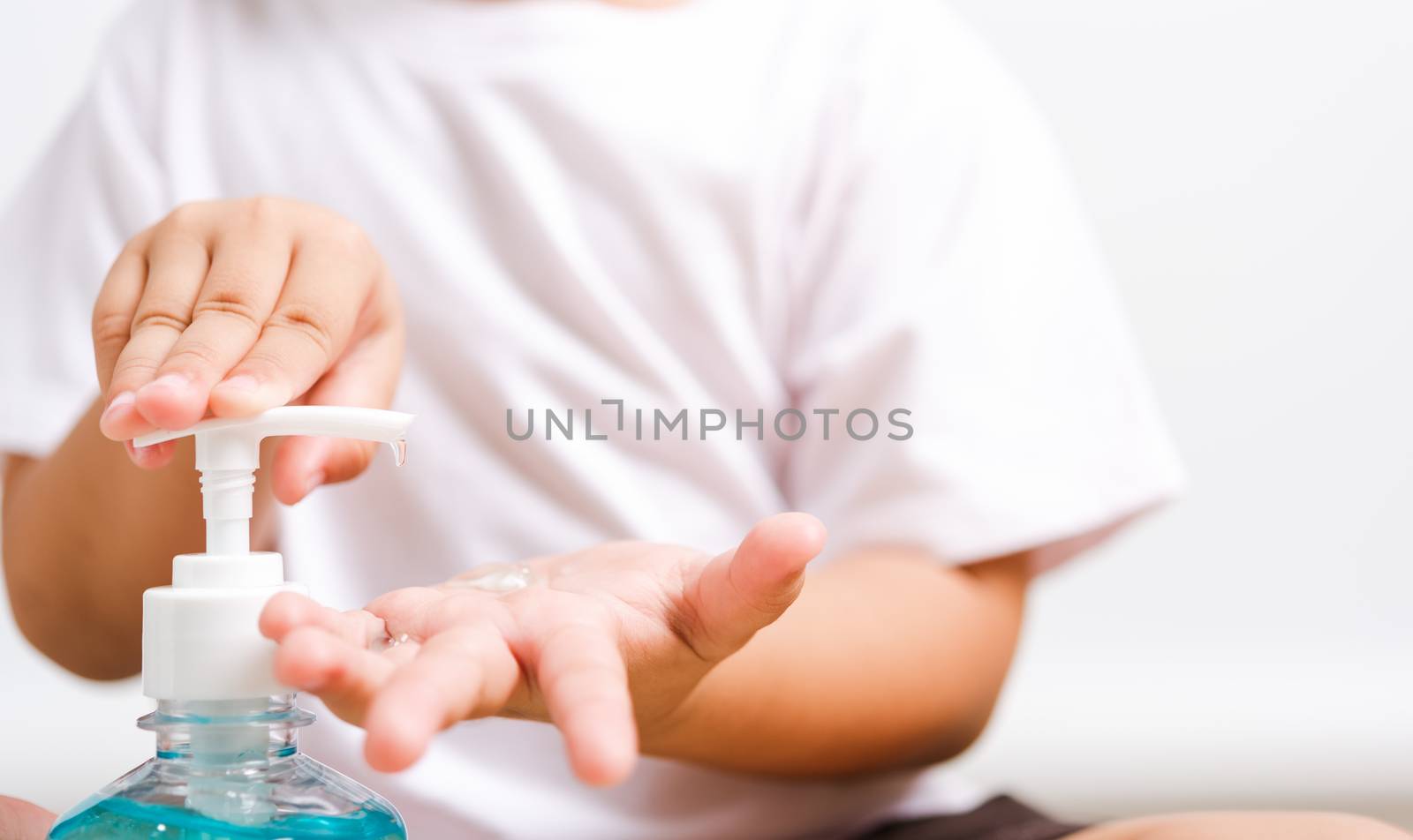 Closeup Asian little child boy sitting applying bottle pump dispenser sanitizer alcohol gel cleaning washing hands yourself, COVID-19 or coronavirus protection concept, isolated on white background with copy space