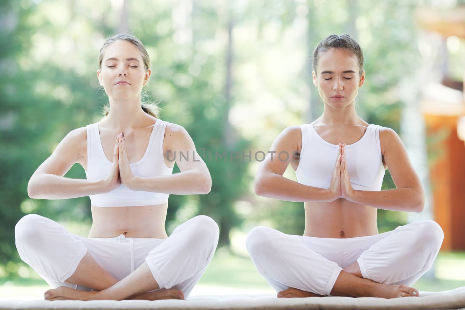 Women in white sportswear sitting in lotus position during group yoga training at park